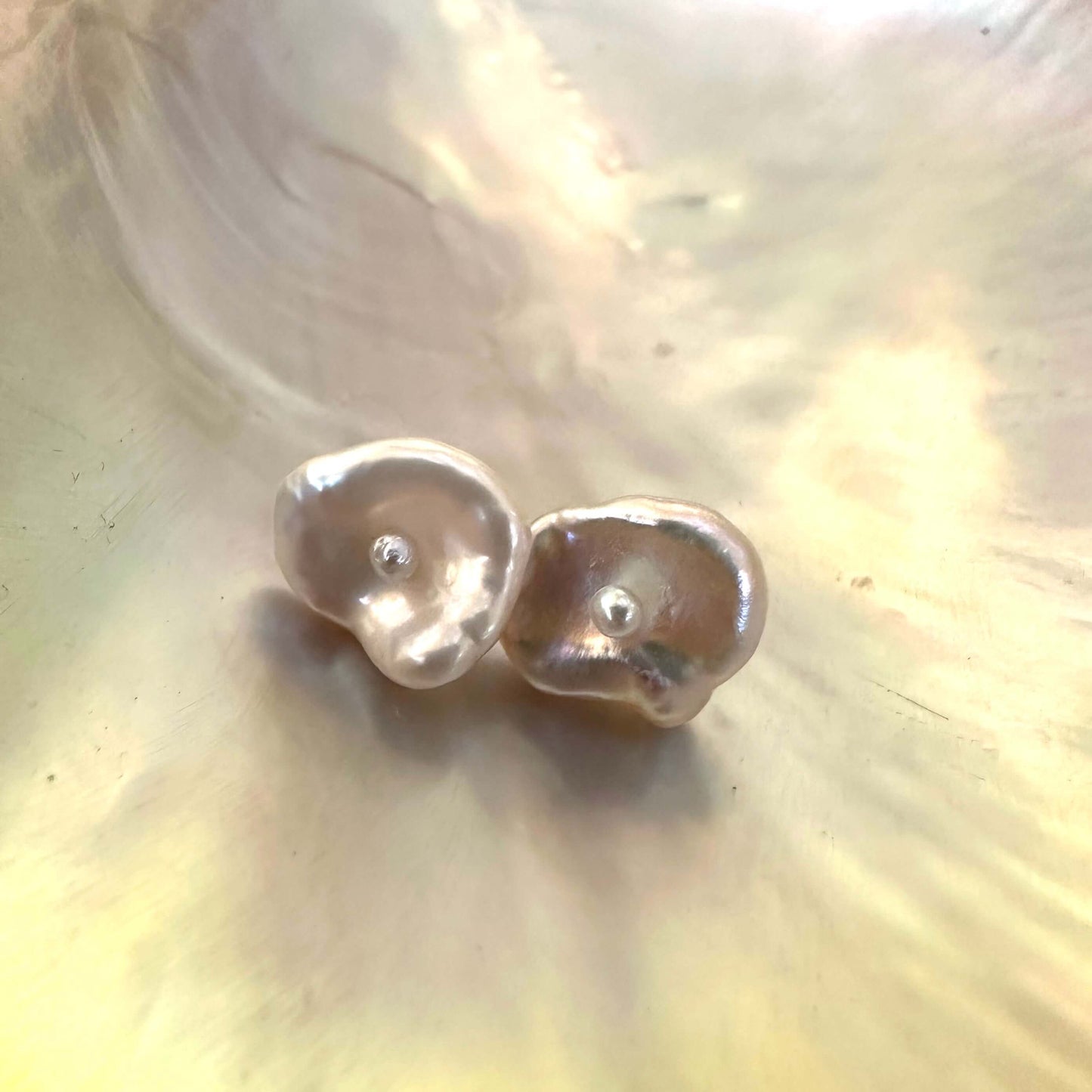 Handmade white flower pearl stud earrings on pearl shell, showing natural irregular shape and elegant gold vermeil posts.