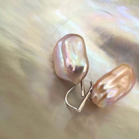 Purple pearl drop earrings with rectangular baroque pearls on white shell, showing pink-lavender hue and natural iridescence.
