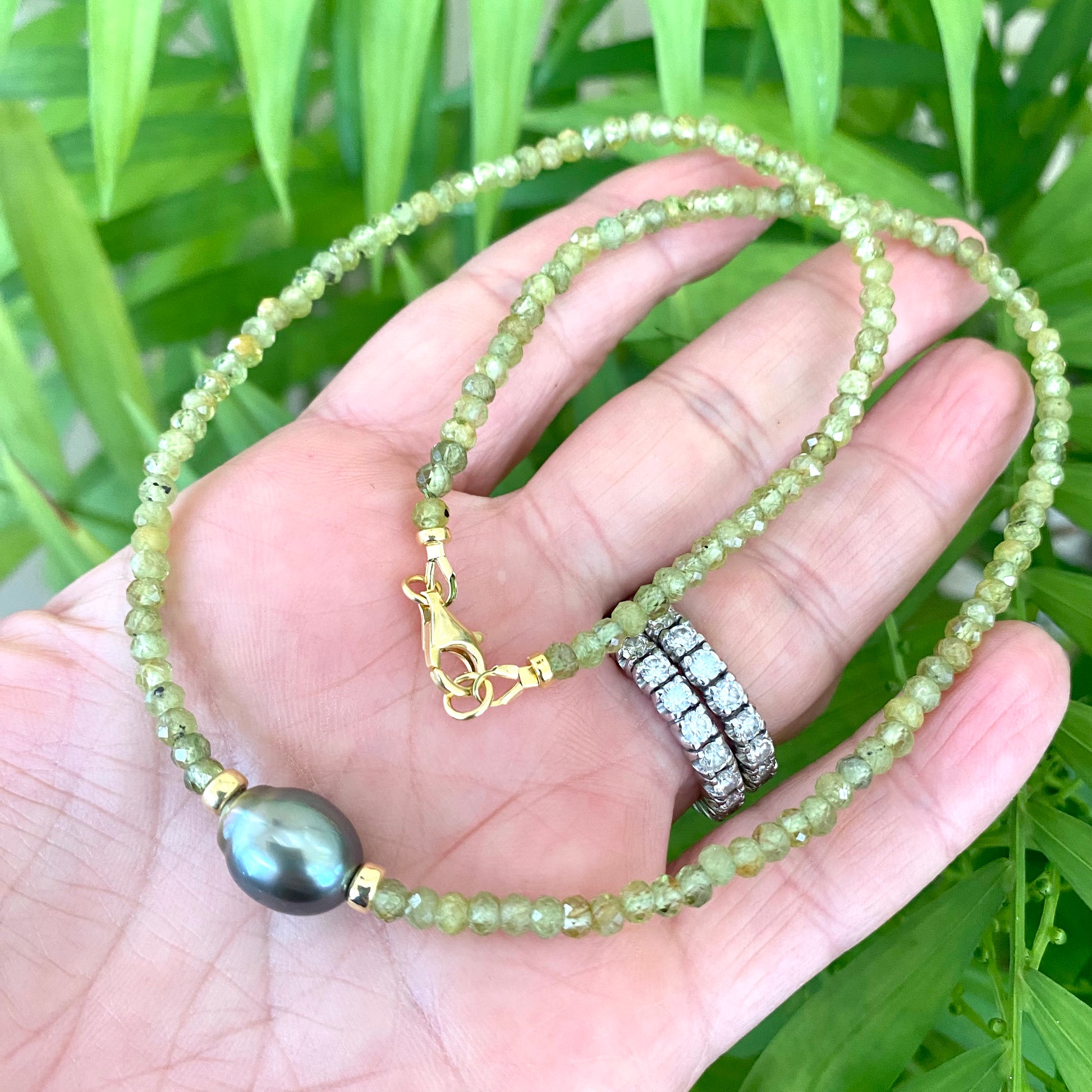 Hand holding a peridot baroque pearl necklace featuring green Peridot beads and a Tahitian Baroque pearl.