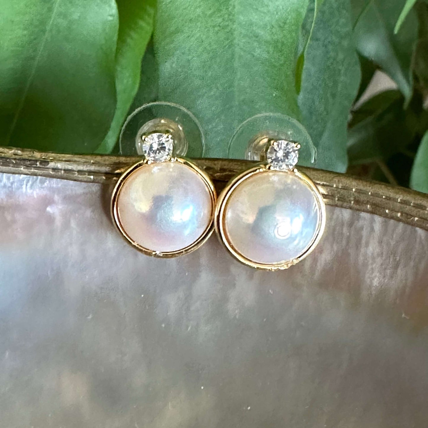 Close-up of Mabe Edison pearl stud earrings with cubic zirconia halo on shell and leaf background