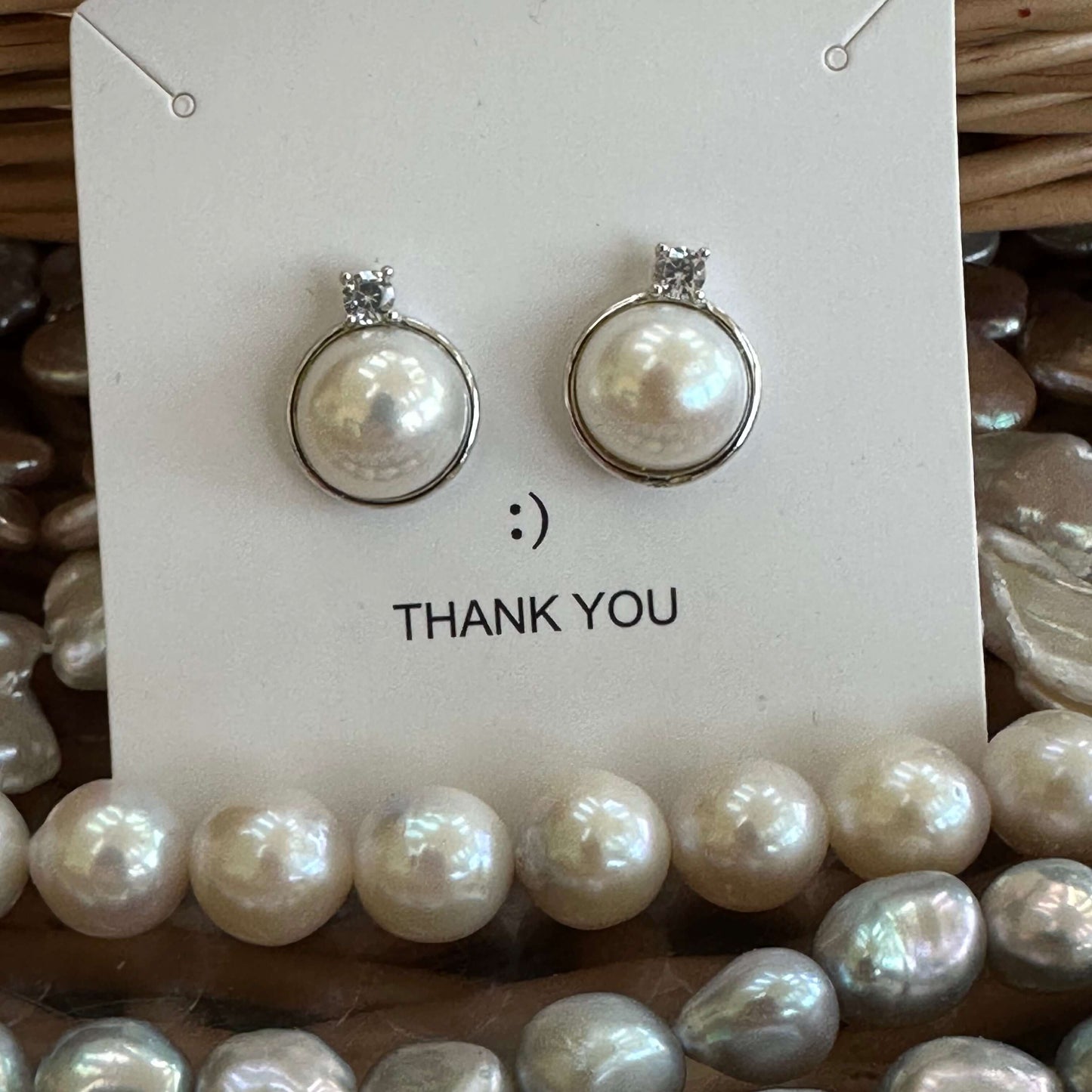 White mabe pearl stud earrings on jewelry package surrounded by pearl necklaces, showcasing coordinated handmade pearl collection.