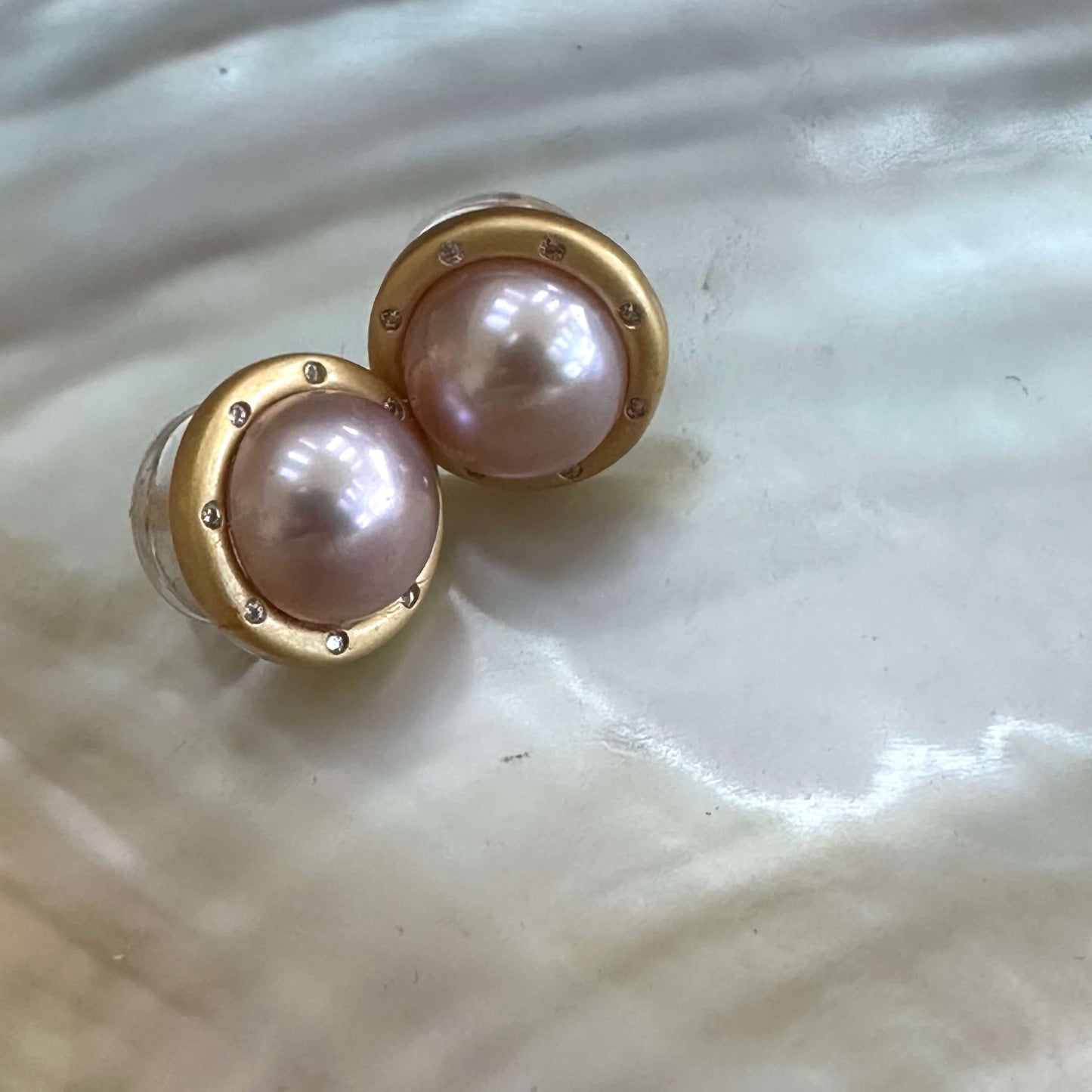 Pink mabe pearl stud earrings with CZ displayed on white pearl shell, showing luminous pink tone and gold vermeil setting.
