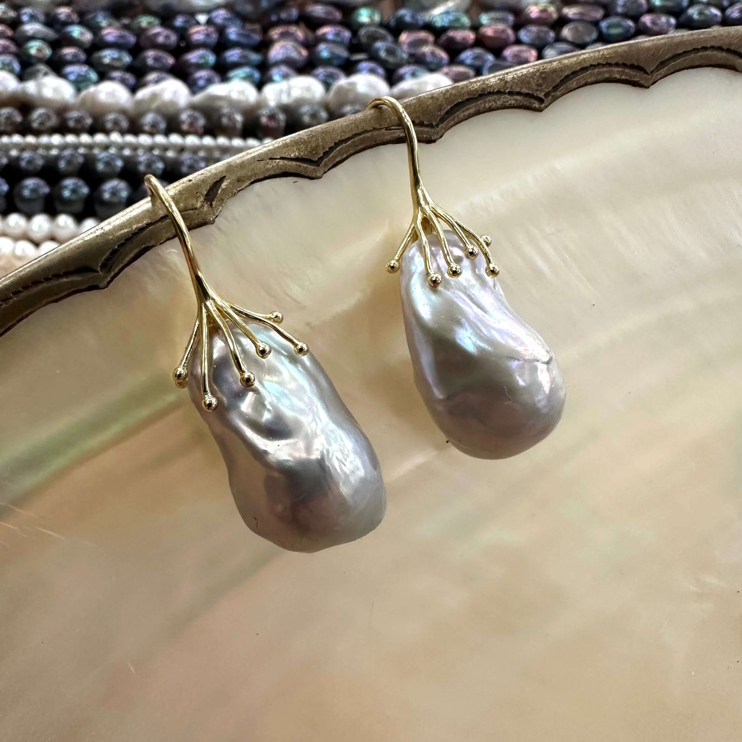 Gold vermeil silver grey baroque pearl drop earrings hanging from white shell, showing elegant dangle and natural pearl sheen.