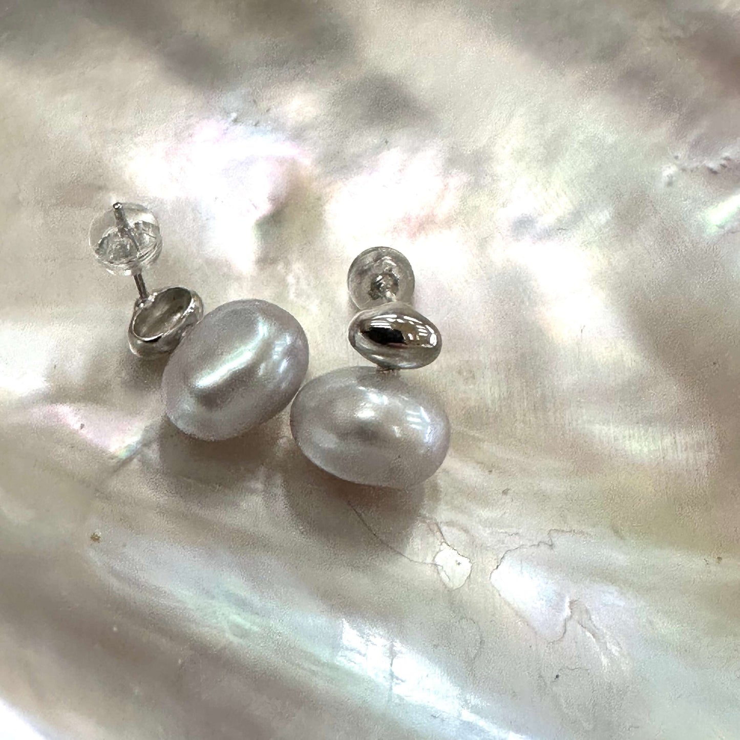 Silver grey nugget pearl stud earrings displayed on white pearl shell, designed and handmade in Canada.
