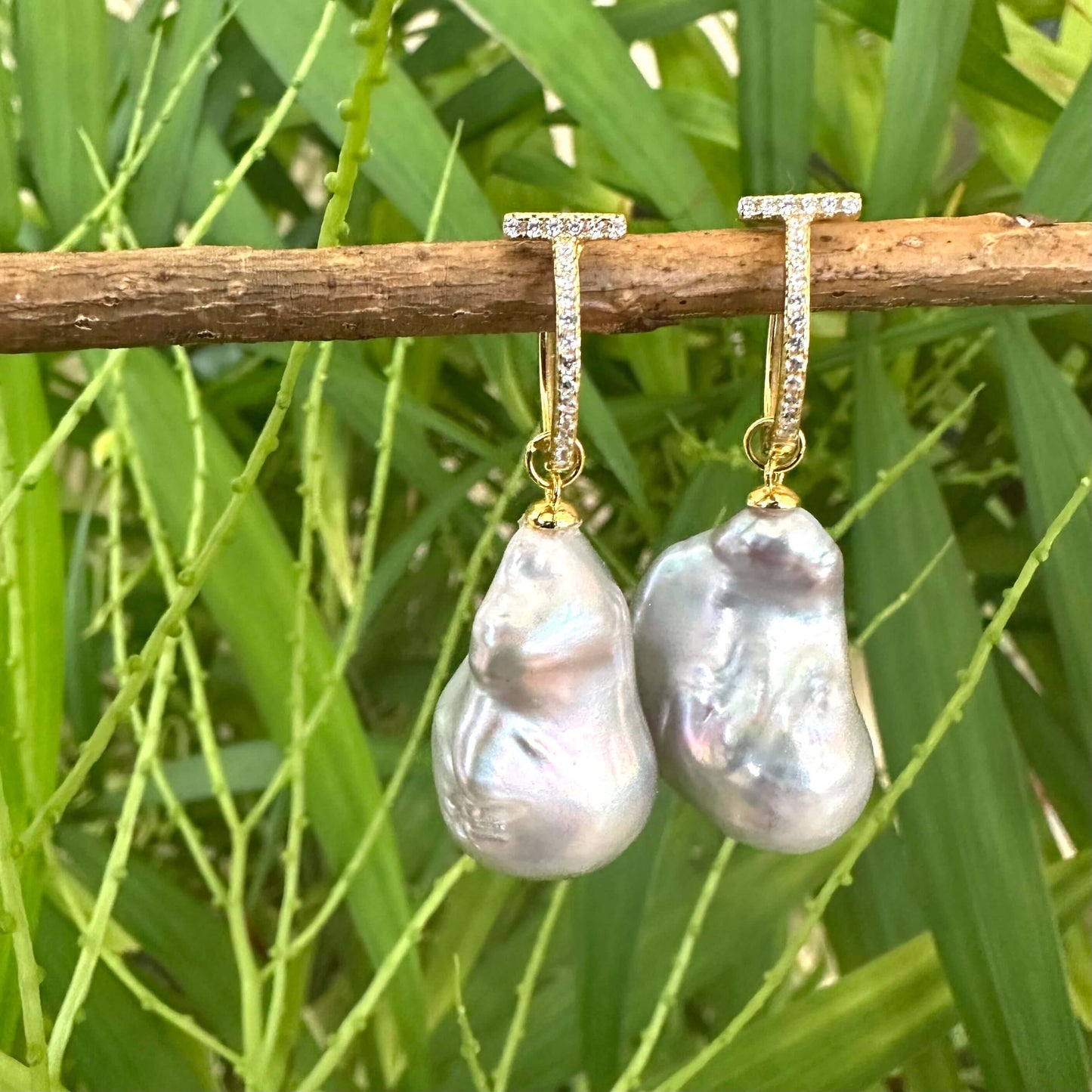 Grey baroque pearl hoop earrings hanging from branch against green leaves, elegant handmade jewelry from Canada.