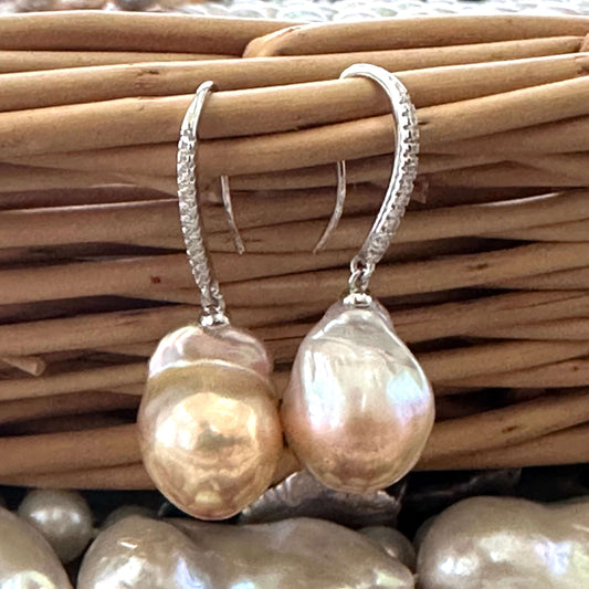 Golden pink baroque pearl dangle earrings resting on wicker basket, sterling silver CZ pavé design handmade in Canada.