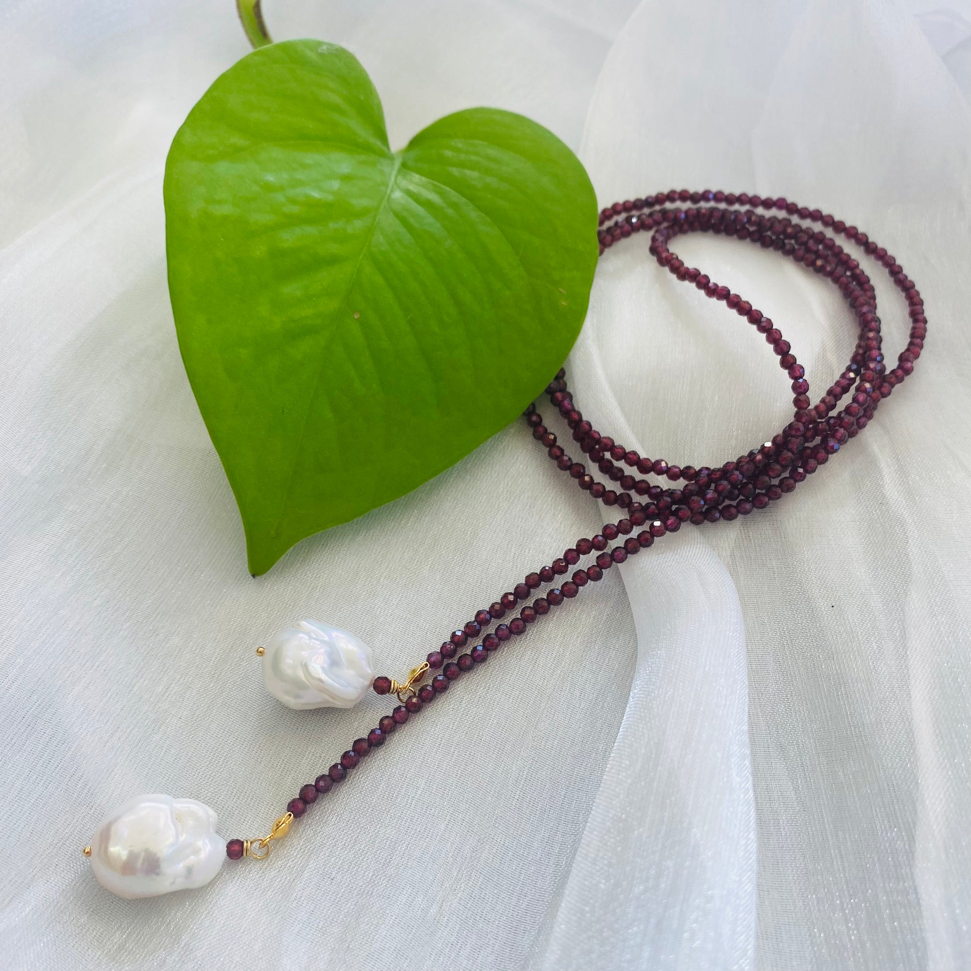 Red Garnet Lariat Necklace flat lay on white fabric with baroque pearl ends visible