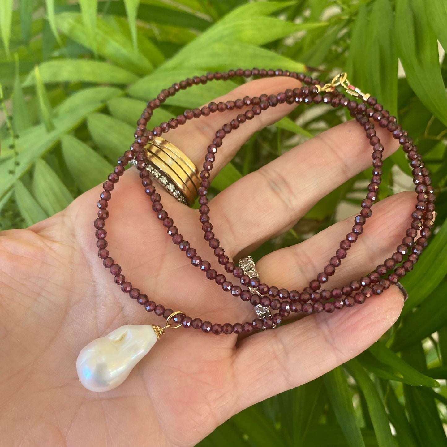 Red garnet baroque pearl necklace with a luminous Baroque pearl pendant displayed on a hand.