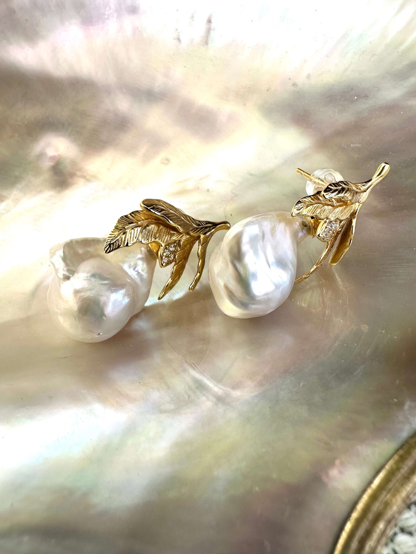 Close-up of handcrafted Baroque Pearl Earrings with oak leaf gold vermeil design displayed on white pearl shell background.