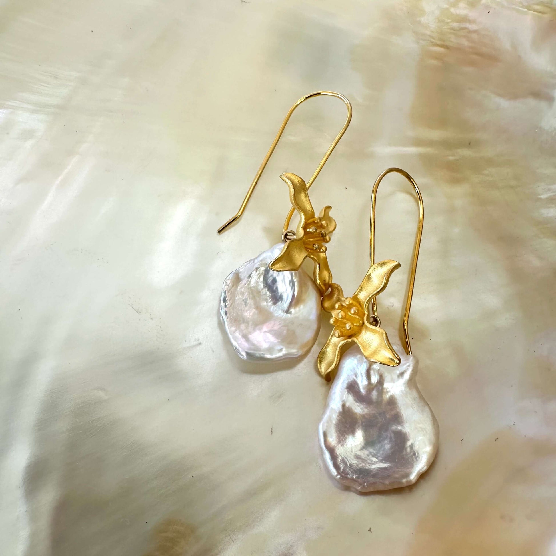 Elegant white Keshi Pearl Earrings with gold vermeil flower hooks resting on pearl shell background.