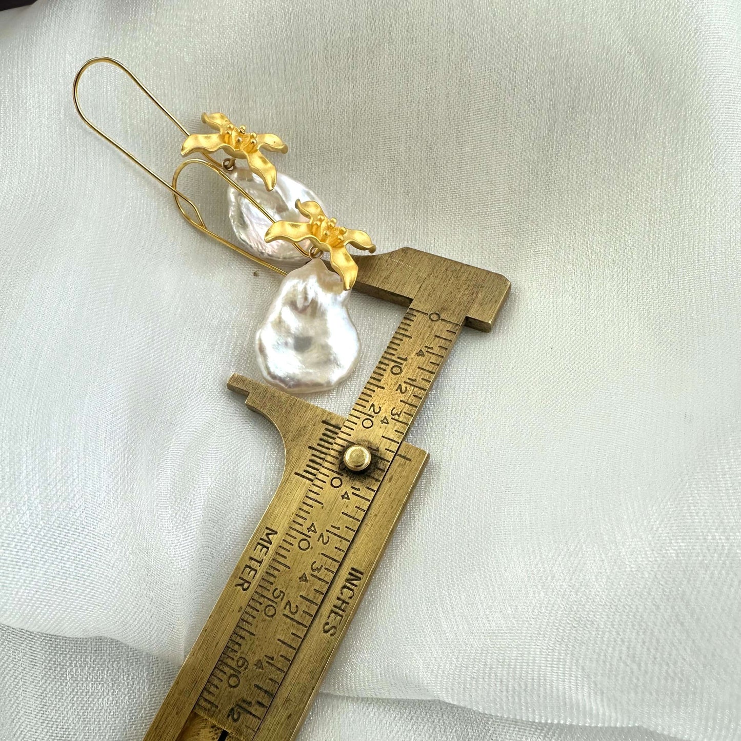 Size reference showing white Keshi pearl from gold vermeil flower earring measured against ruler on white background.