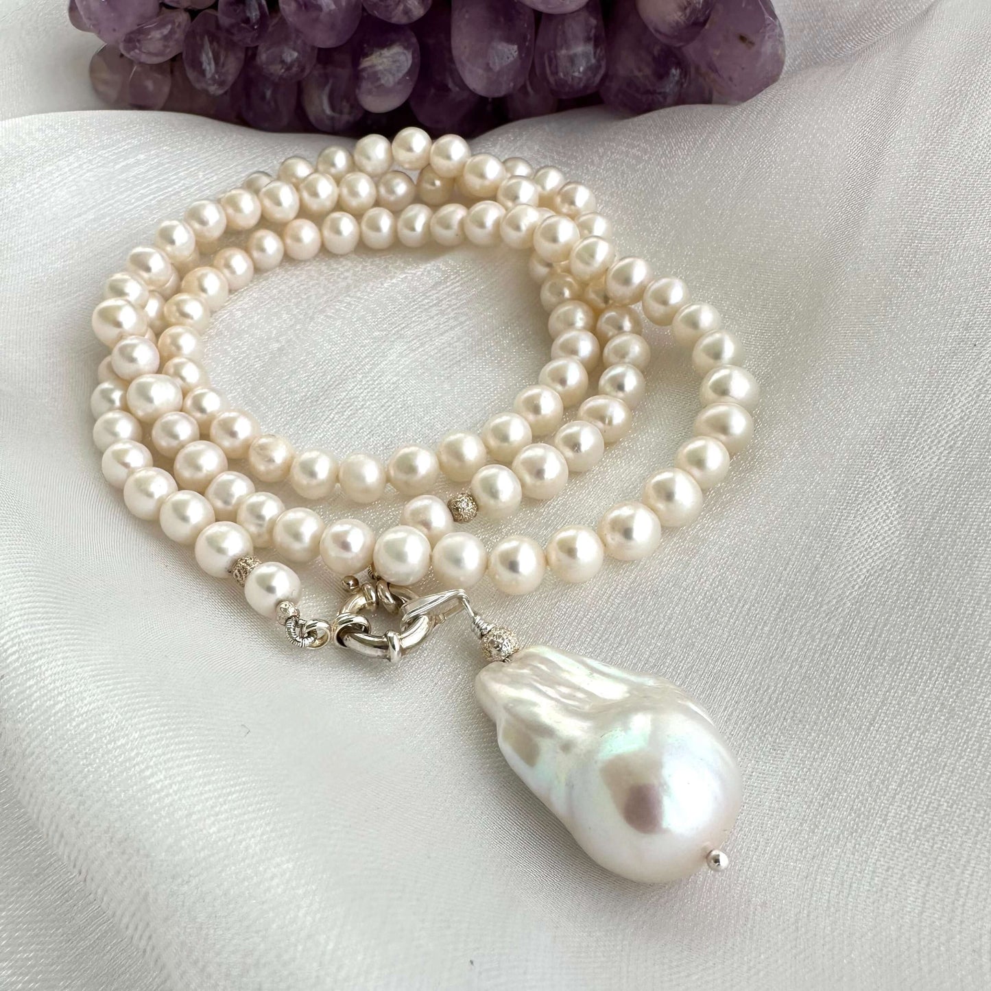 Close-up of white pearl necklace with baroque pendant on white background
