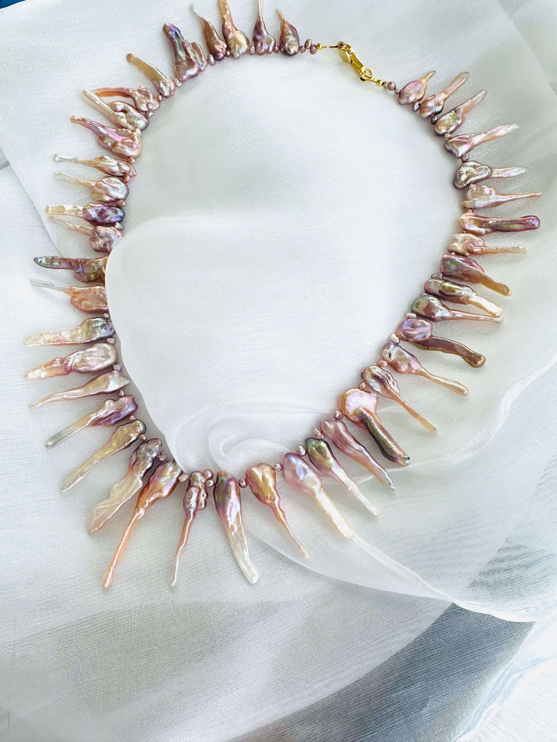 Pink Biwa pearl necklace displayed on soft white fabric background, handmade jewelry