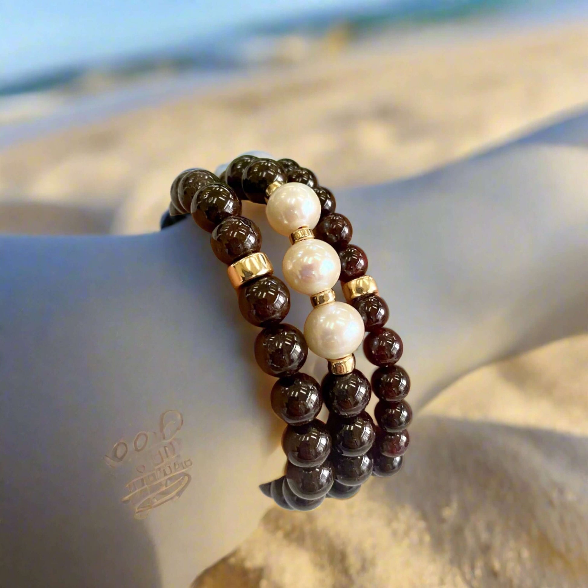 Dark Red Garnet Bracelet worn on mannequin’s arm against beach view – outdoor scene