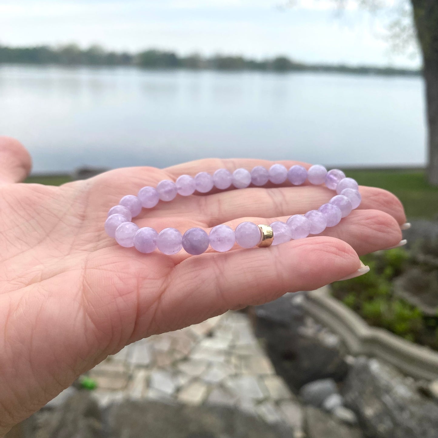 Lavender Amethyst Bracelet held in hand – purple gemstone detail by water