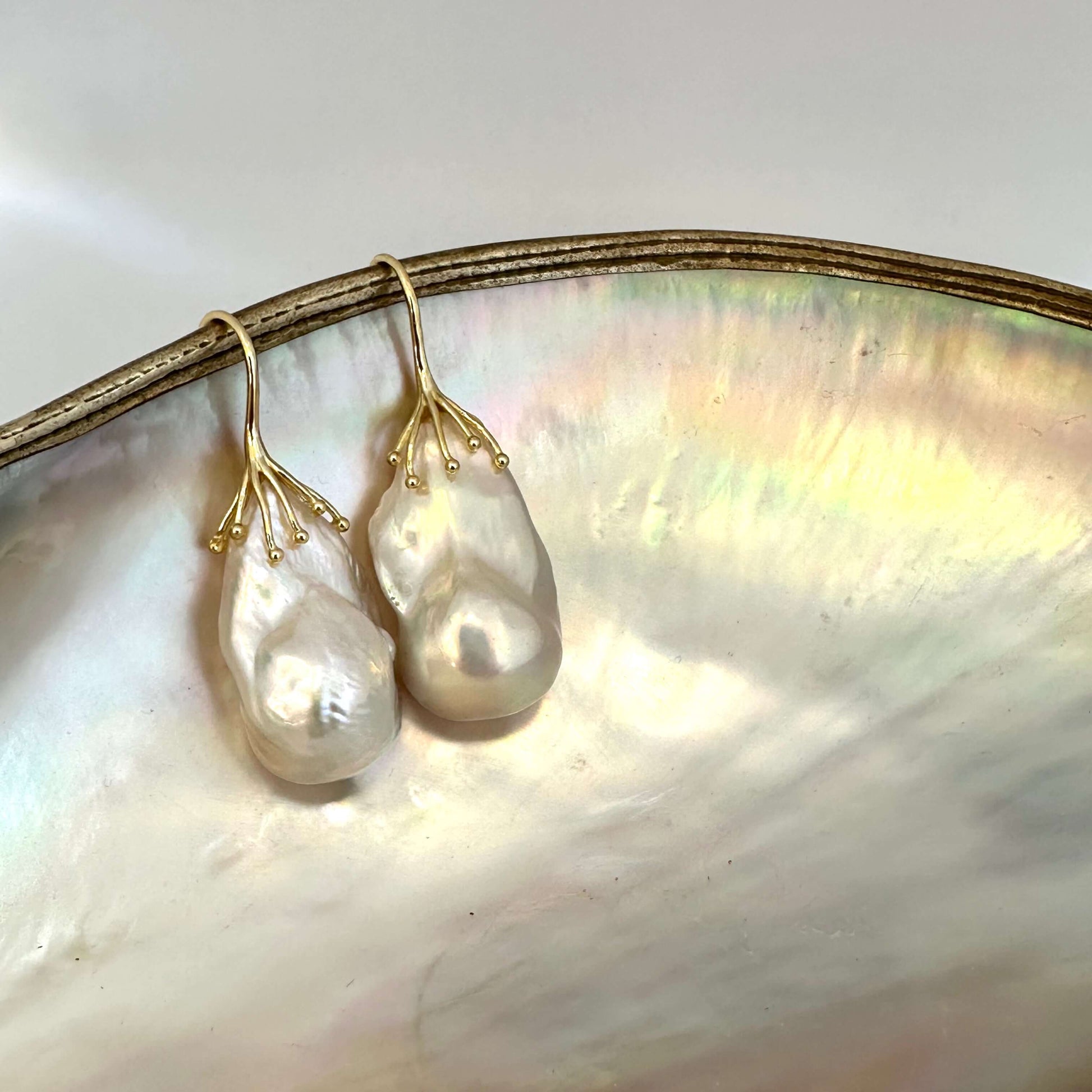 Gold baroque pearl drop earrings close-up on white pearl backdrop – lustrous handcrafted jewelry