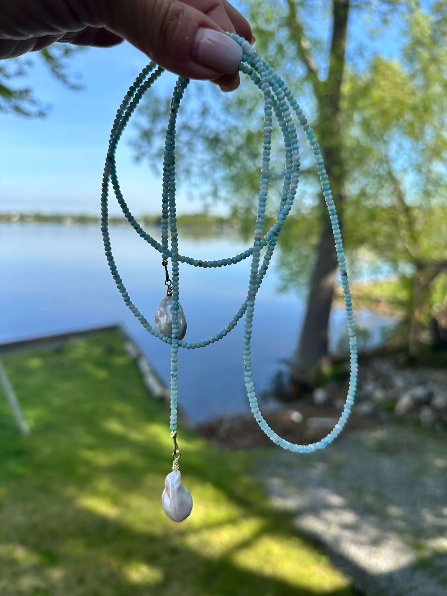 Blue Larimar Lariat Necklace held against lake and grass background — natural gemstone and pearl necklace handcrafted by Loulia Pearl Jewelry