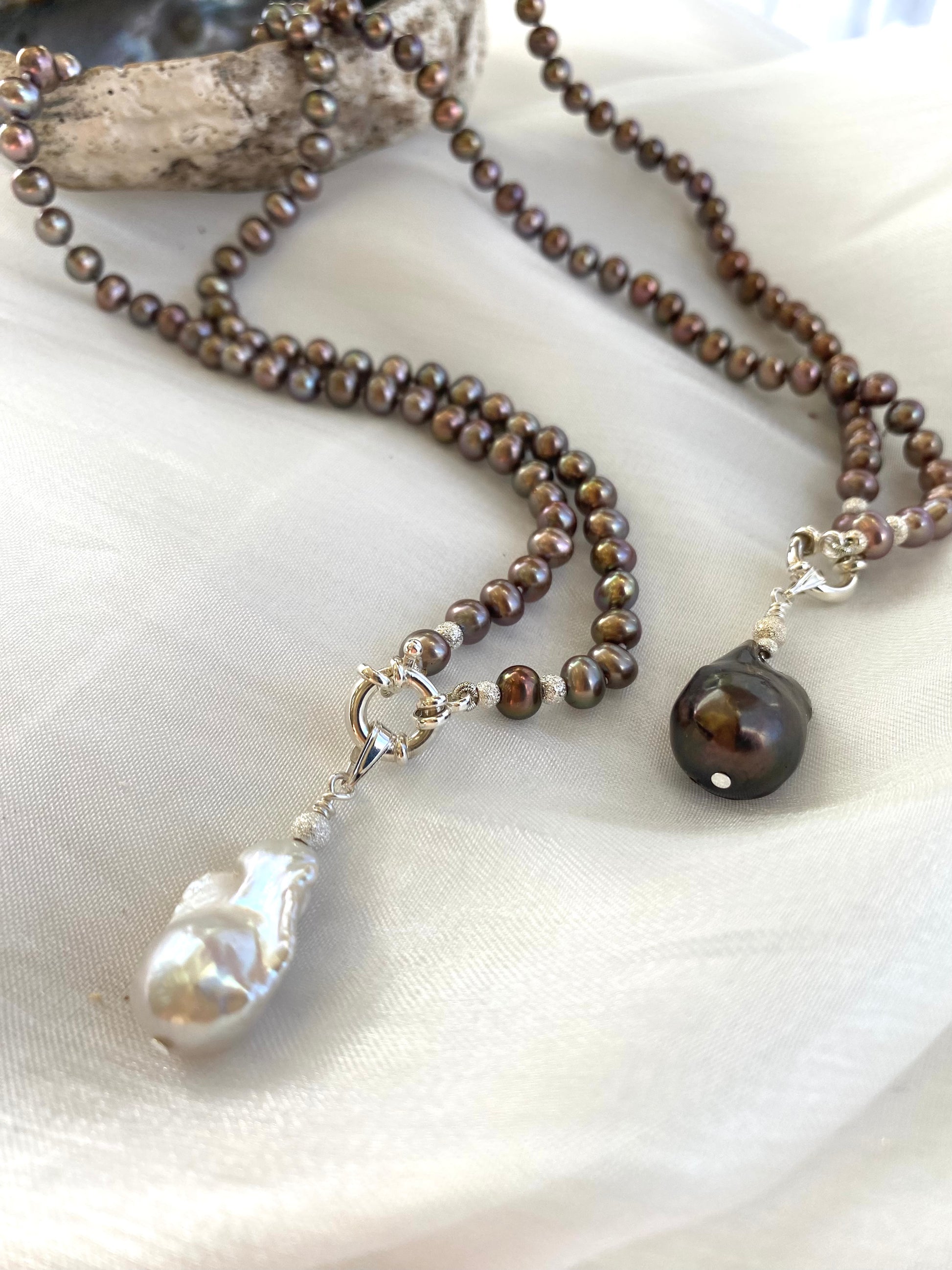 White and brown baroque pendant bronze pearl necklaces side by side on white cloth, showing variant colors and handmade quality.