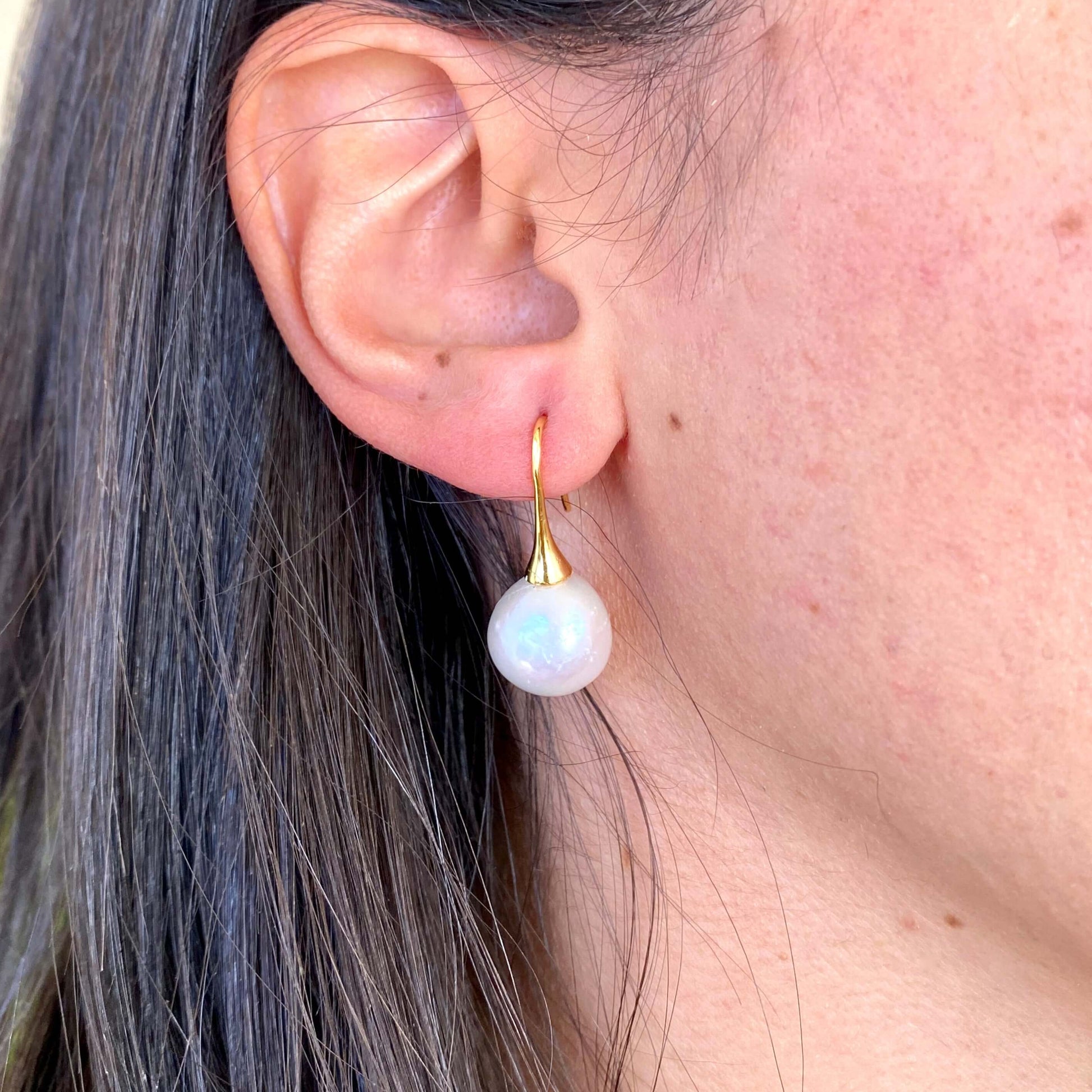 Model wearing white pearl drop earrings with large Edison pearls and gold hooks, showing elegant side profile and soft glow.