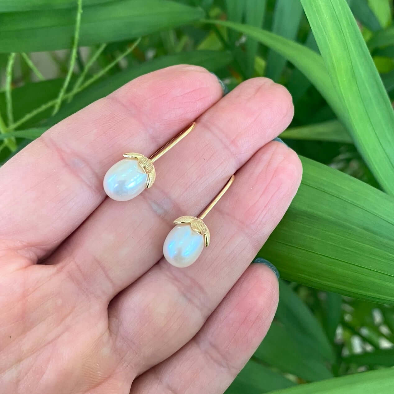 Rice Pearl Earrings – gold earrings held by hand against green leaf background