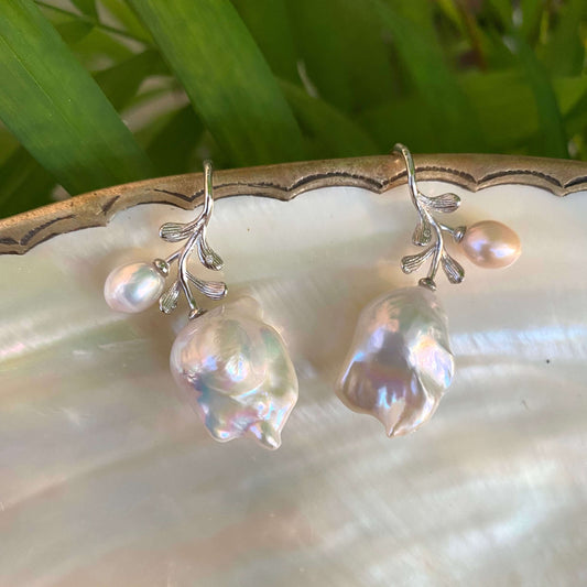 Baroque pearl earrings in silver displayed on pearl shell and green leaf backdrop