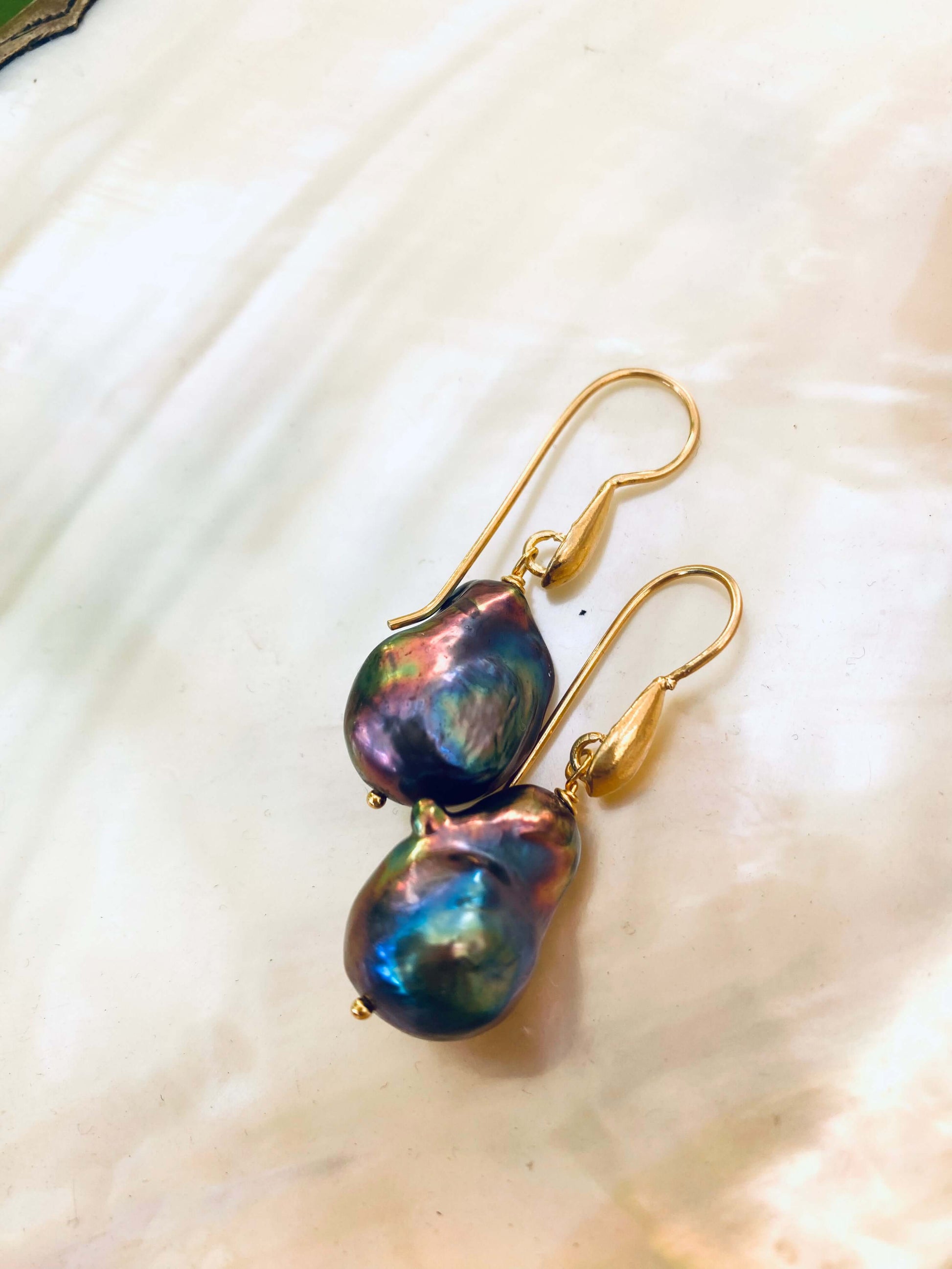 Black peacock baroque pearl drop earrings with iridescent finish on white shell background