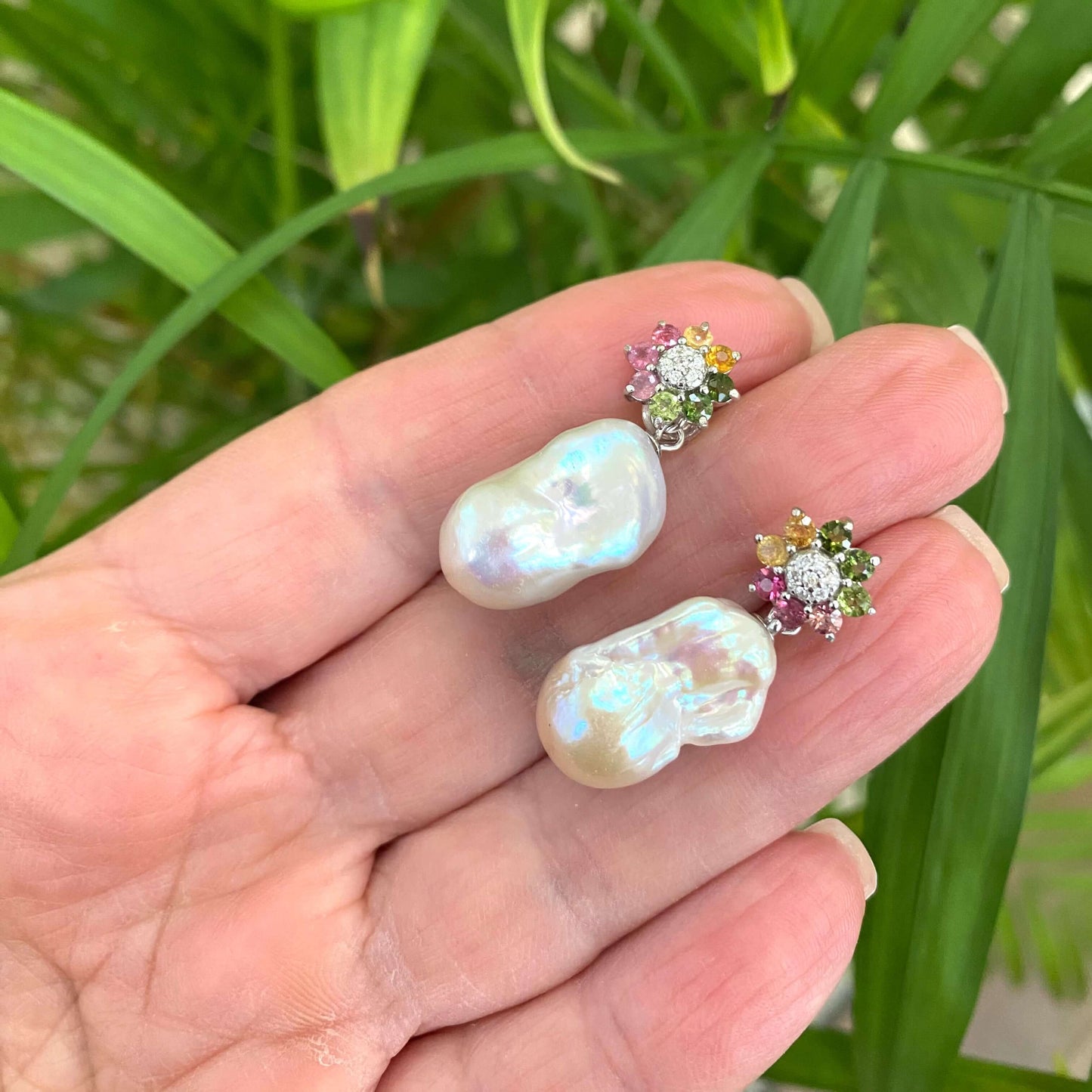 Tourmaline pearl earrings held in hand for size comparison against green leaf background