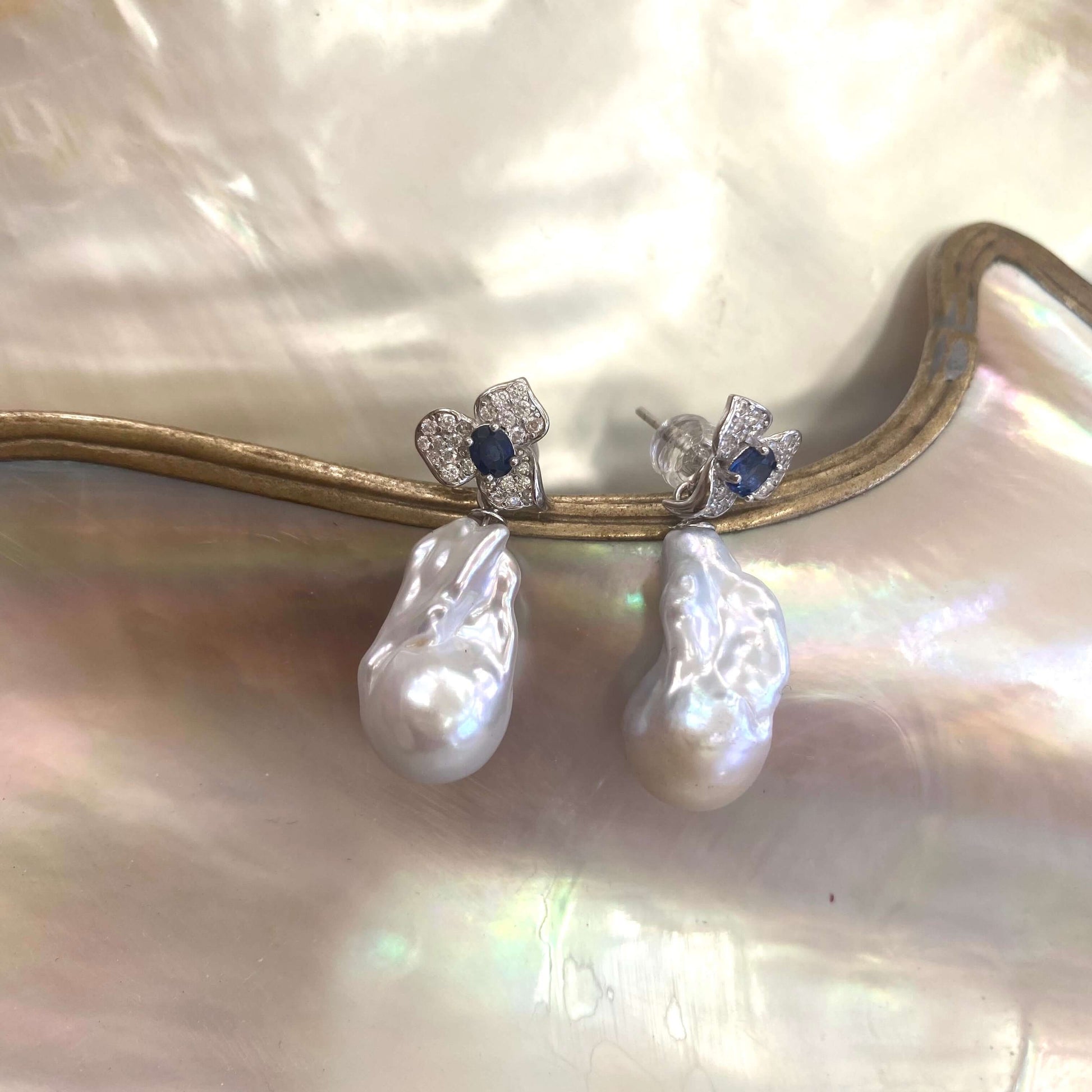 Close view of sapphire and emerald stud earrings with pearl drops on shell background