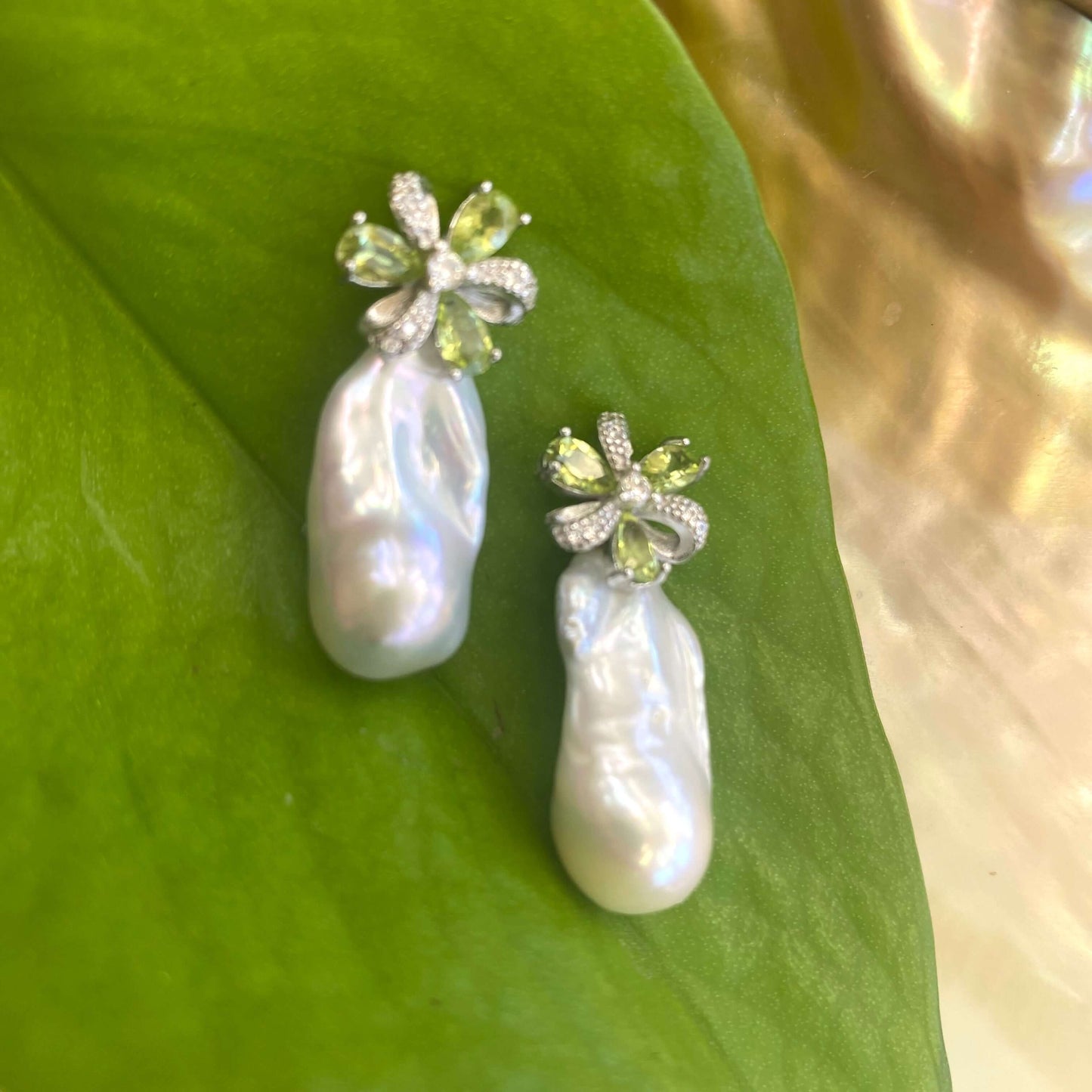 Peridot stud earrings with baroque pearl drops on green leaf backdrop