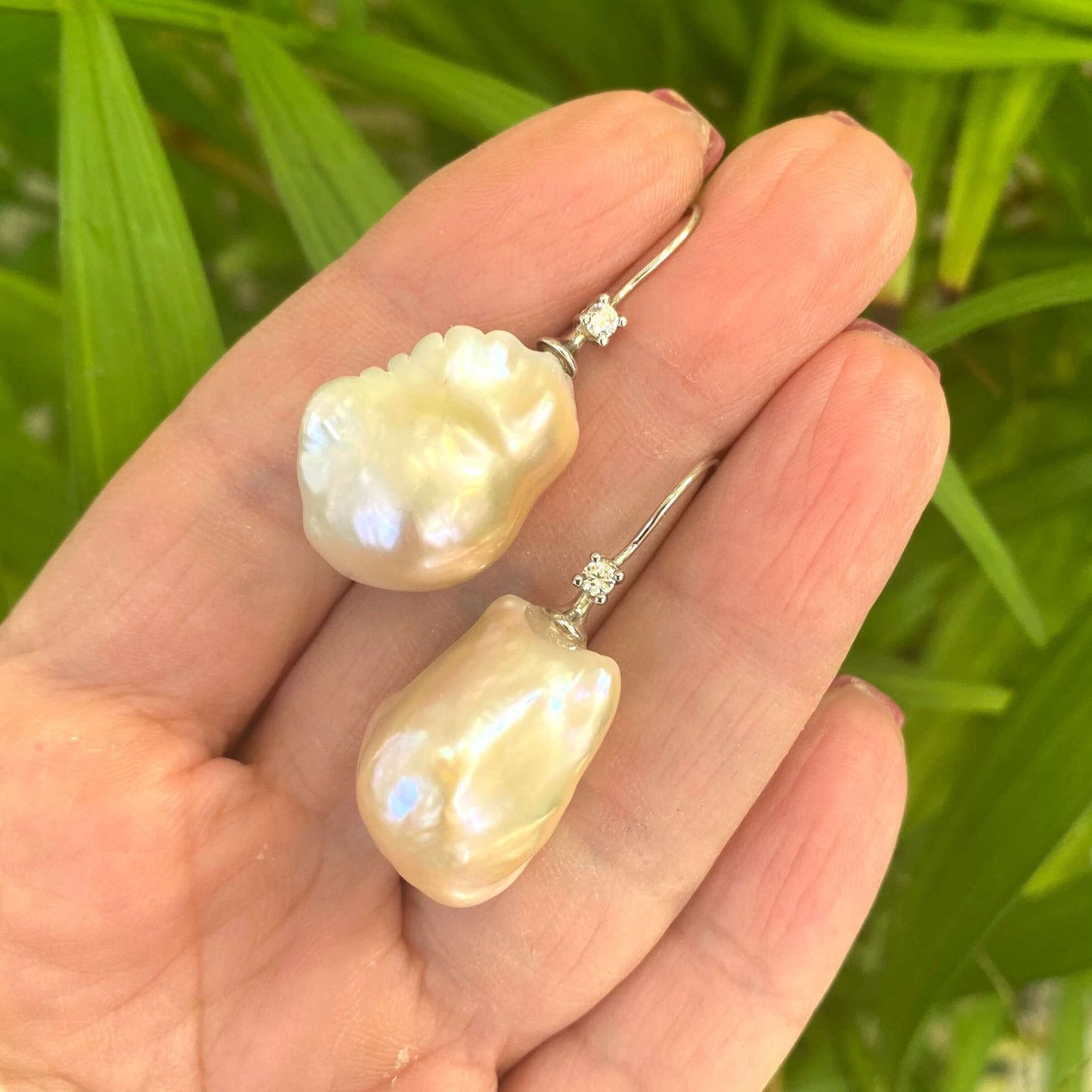 Golden Baroque Pearl Earrings – held by hand against green leaf backdrop