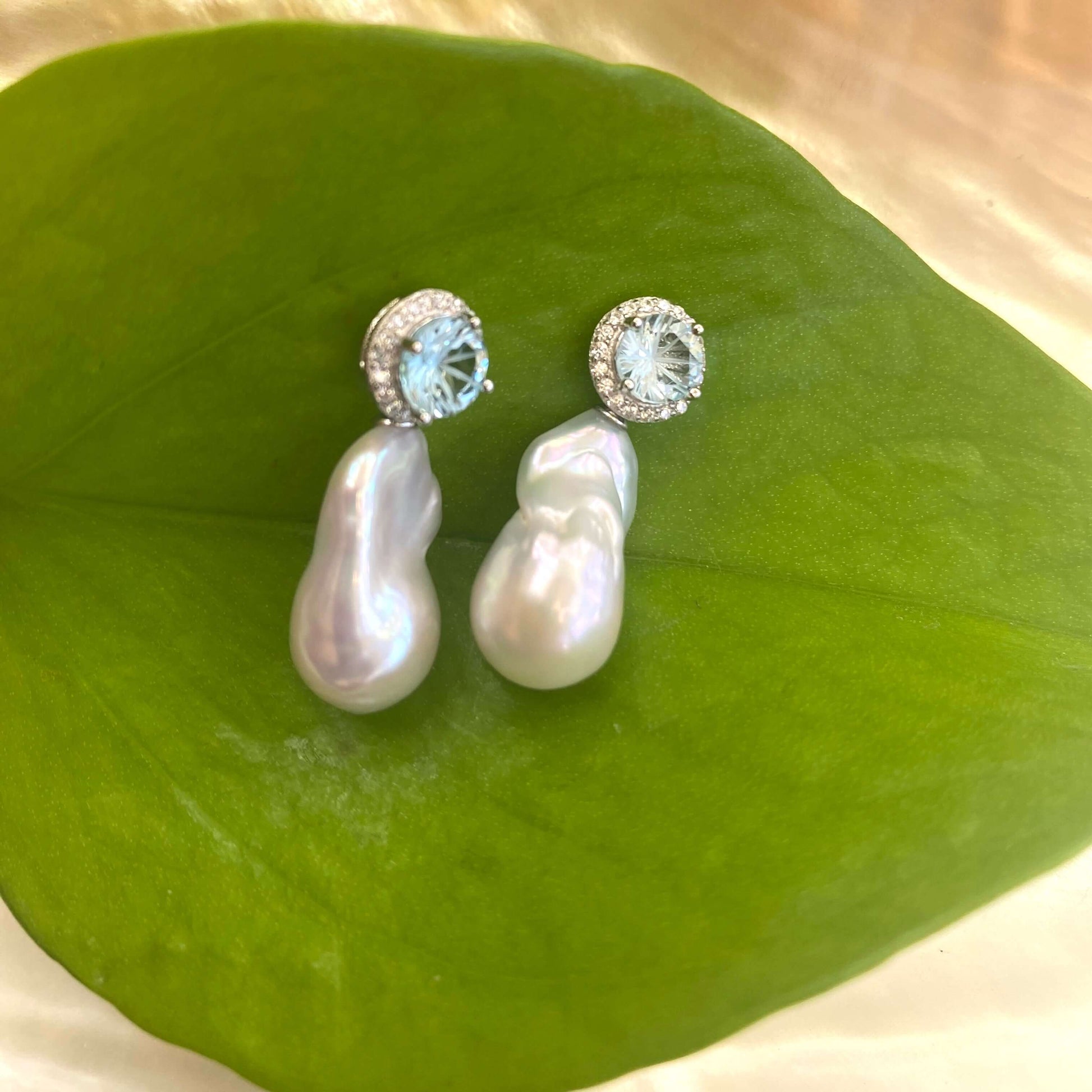 Blue topaz pearl drop earrings with removable baroque pearls against green leaf