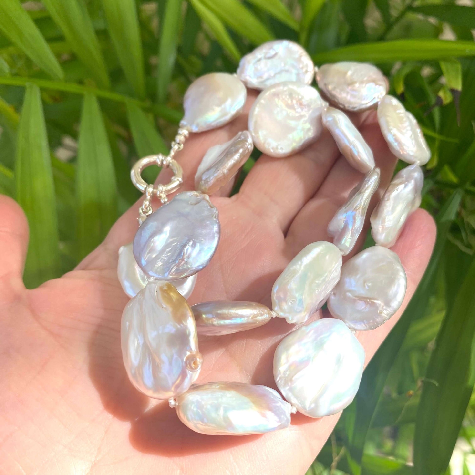 Close view of large coin pearl necklace with natural pearls on leaf backdrop