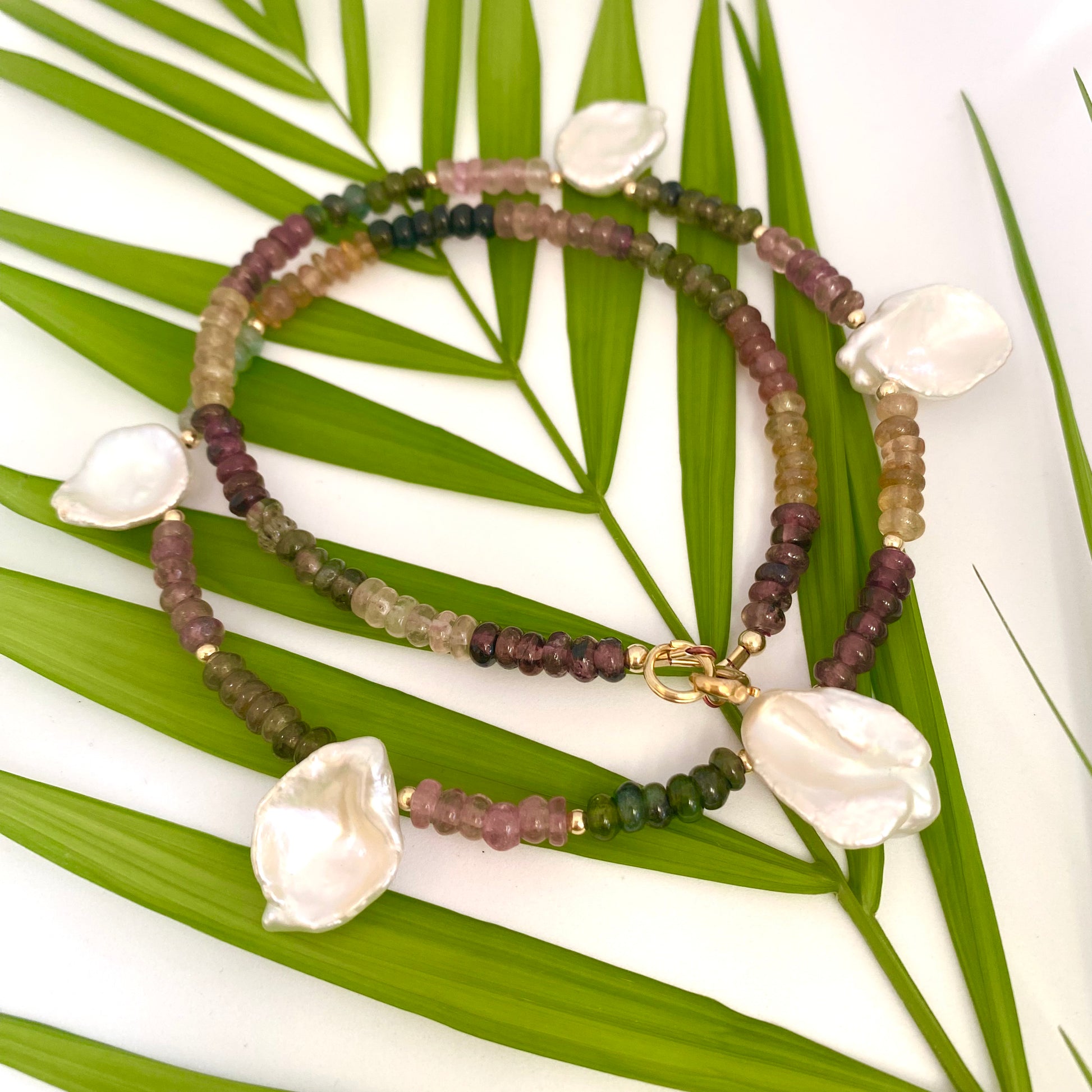 Handcrafted multi tourmaline and keshi pearl necklace against leaf and white background, artisan jewelry.
