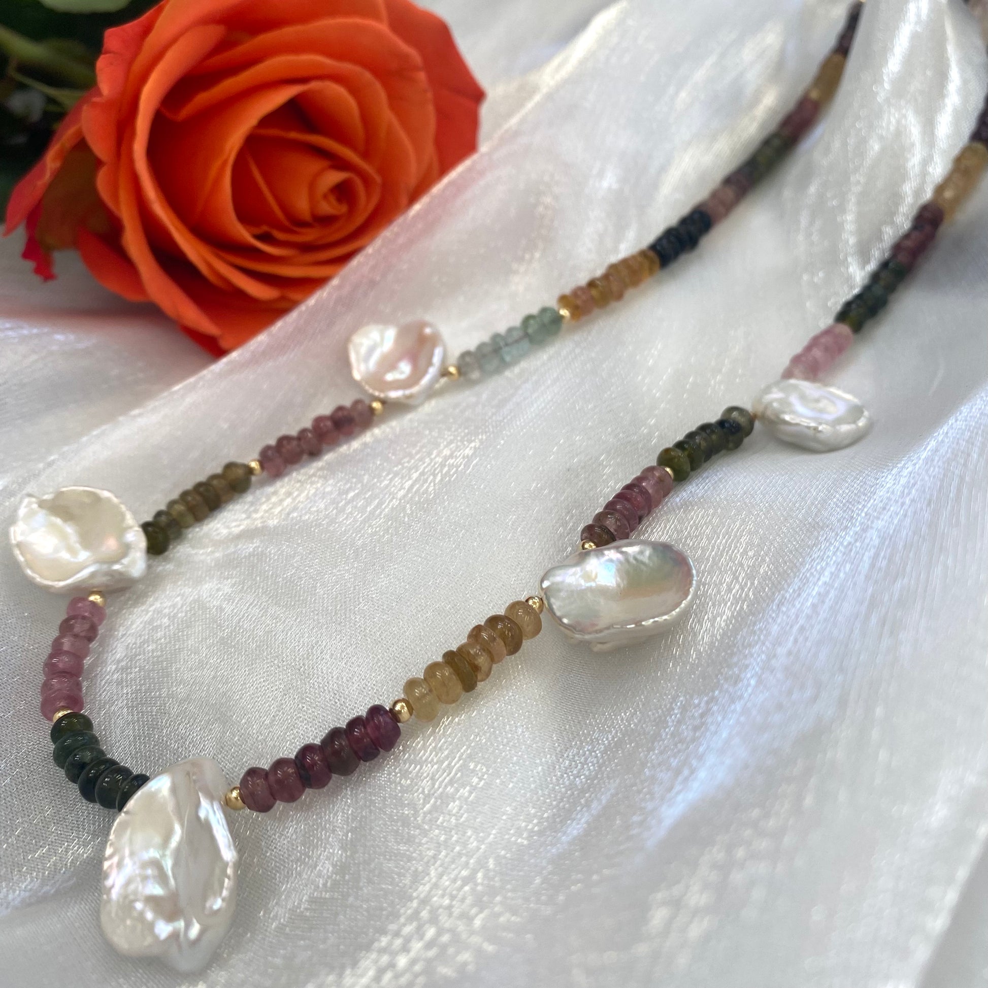 Close-up of multi tourmaline and keshi pearl necklace on white background, 14K gold accents.