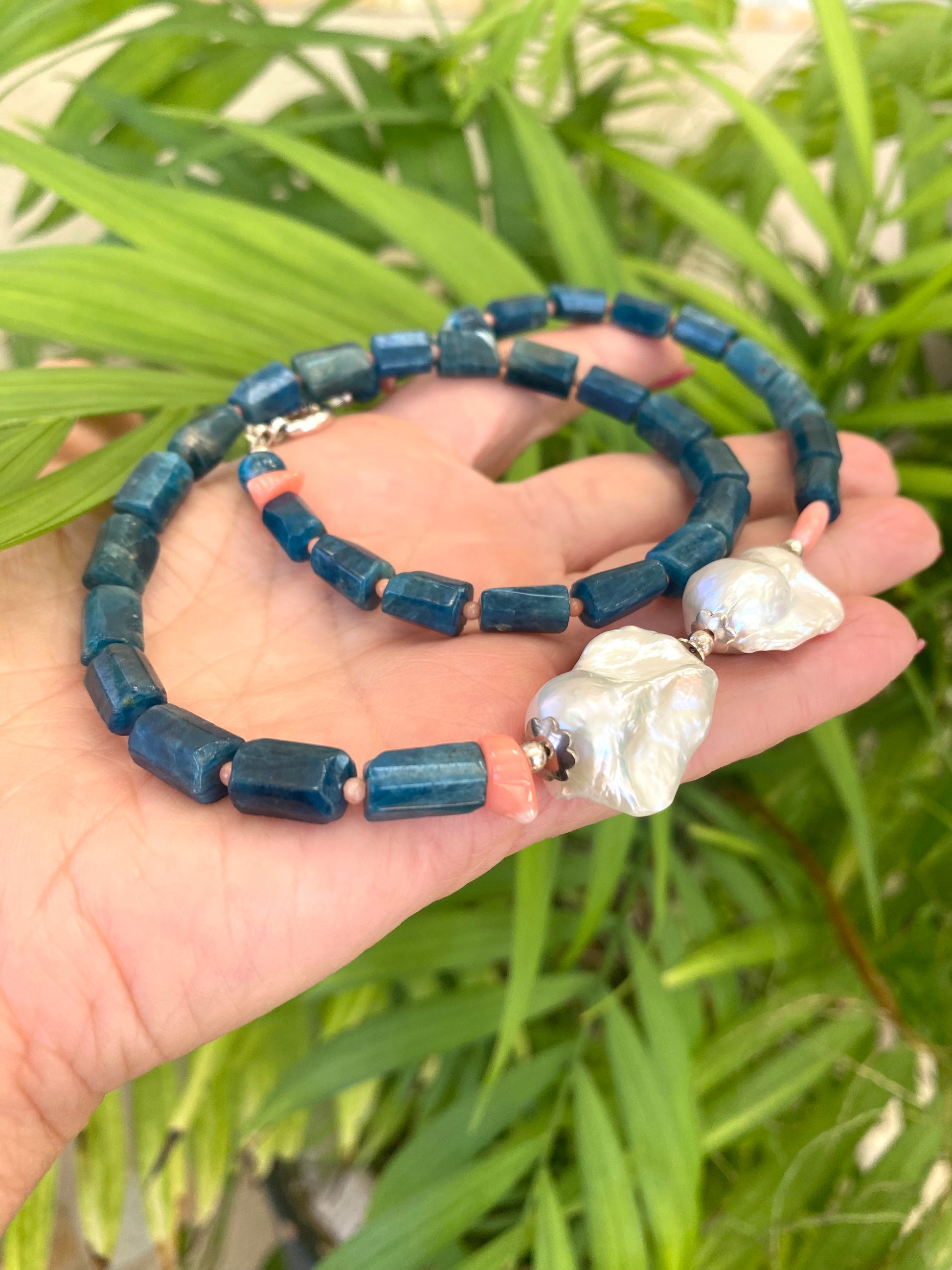 Blue apatite coral pearl necklace held in hand against leafy green backdrop — colorful handcrafted gemstone jewelry by Loulia Pearl Jewelry