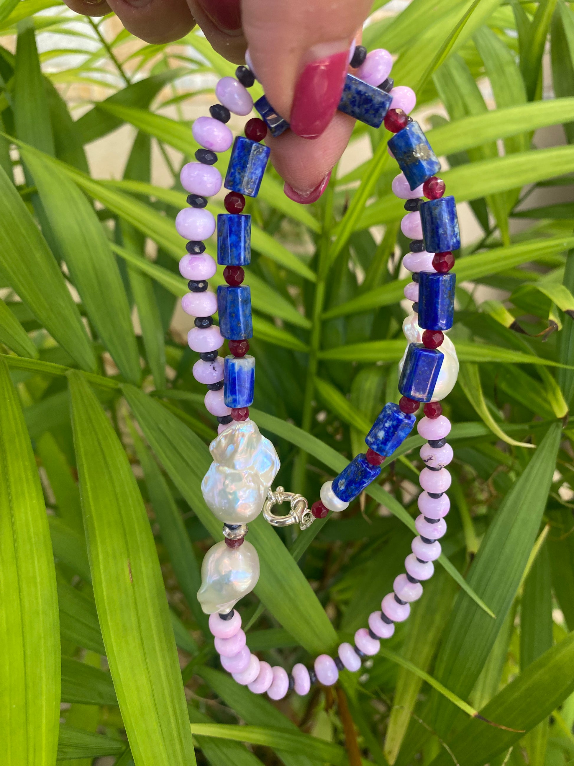 Lapis lazuli opal agate pearl necklace held against green leafy background — handcrafted gemstone and baroque pearl jewelry by Loulia Pearl Jewelry