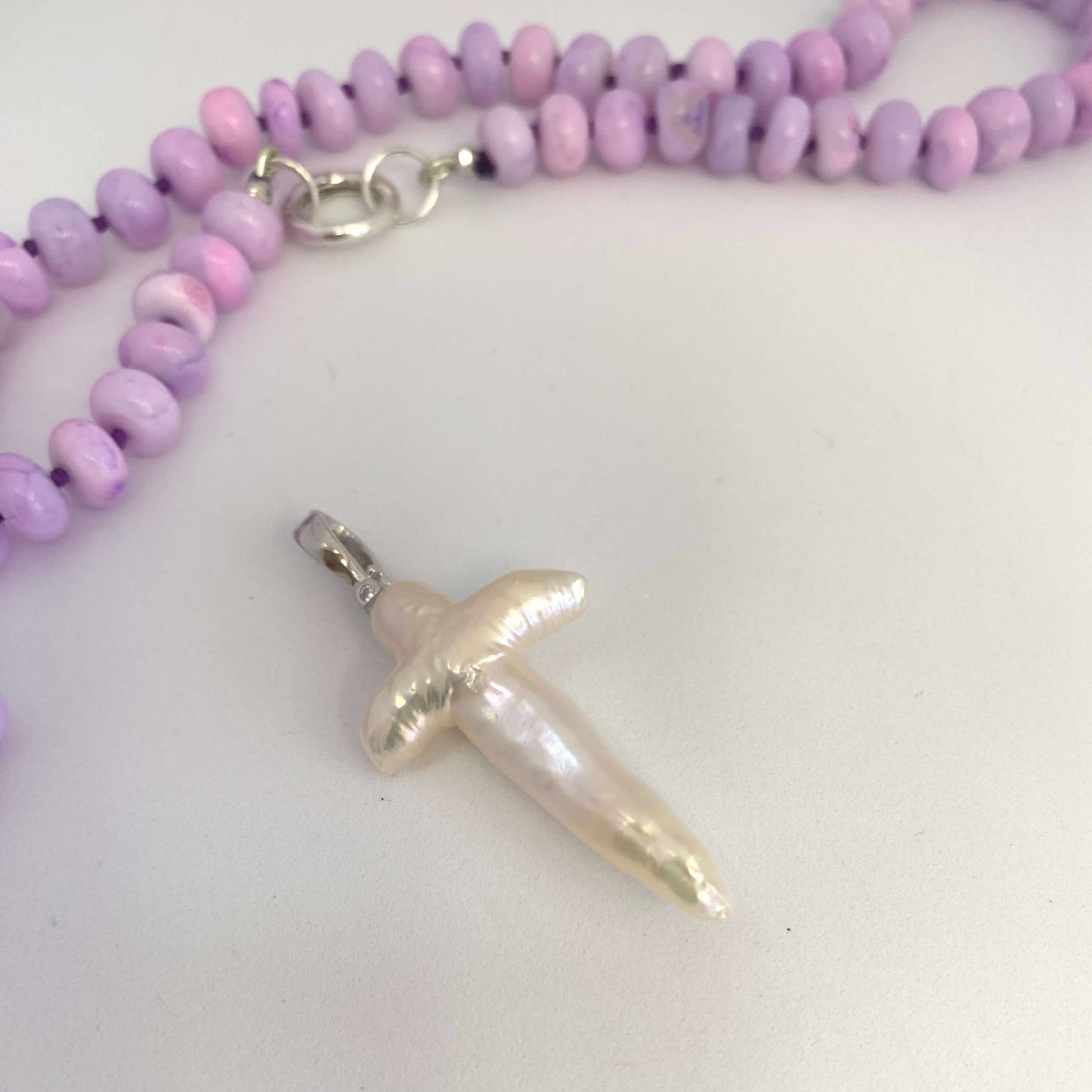 Baroque pearl cross pendant close-up on white background, luminous handcrafted detail.