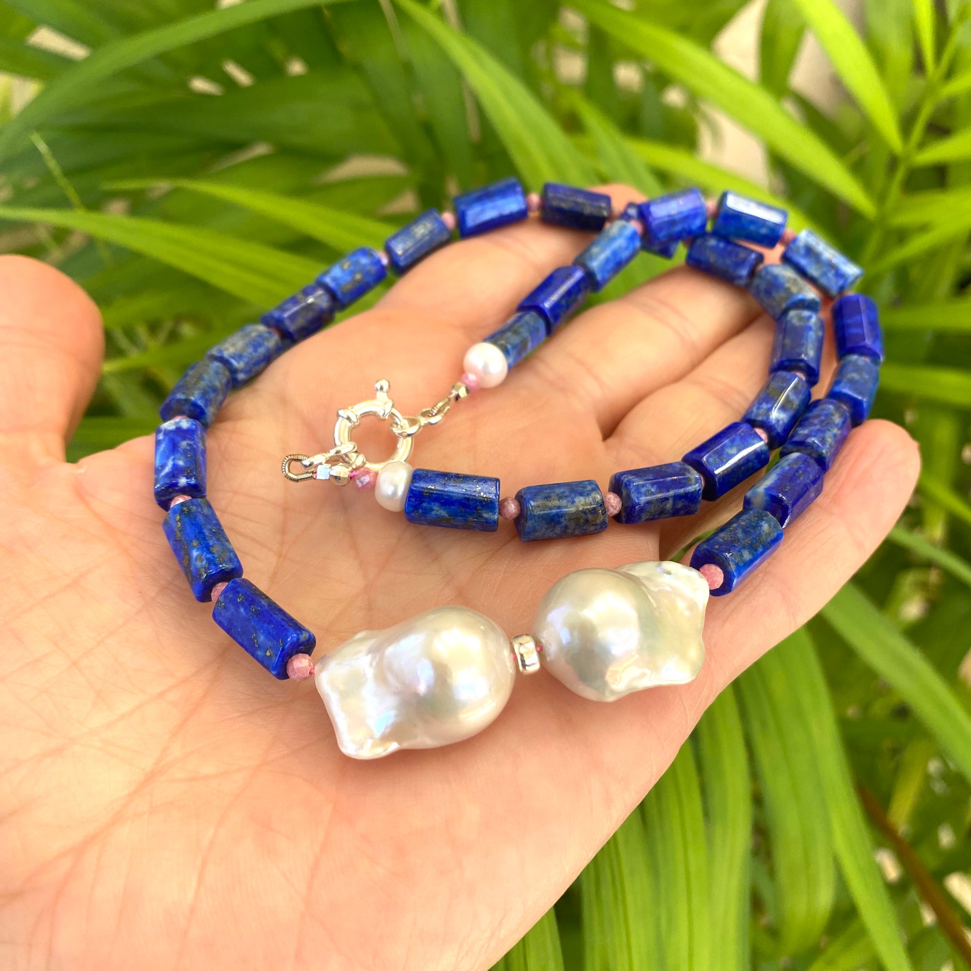 Lapis Lazuli Pink Rhodonite Baroque Pearl Necklace held in hand against green leaves — handcrafted gemstone and pearl jewelry by Loulia Pearl Jewelry