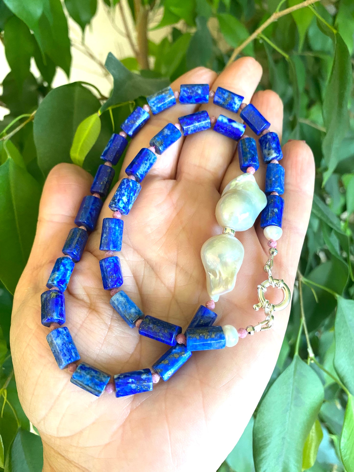 Handcrafted Lapis Lazuli Pink Rhodonite Baroque Pearl Necklace photographed outdoors with leafy green backdrop — natural gemstone jewelry by Loulia Pearl Jewelry