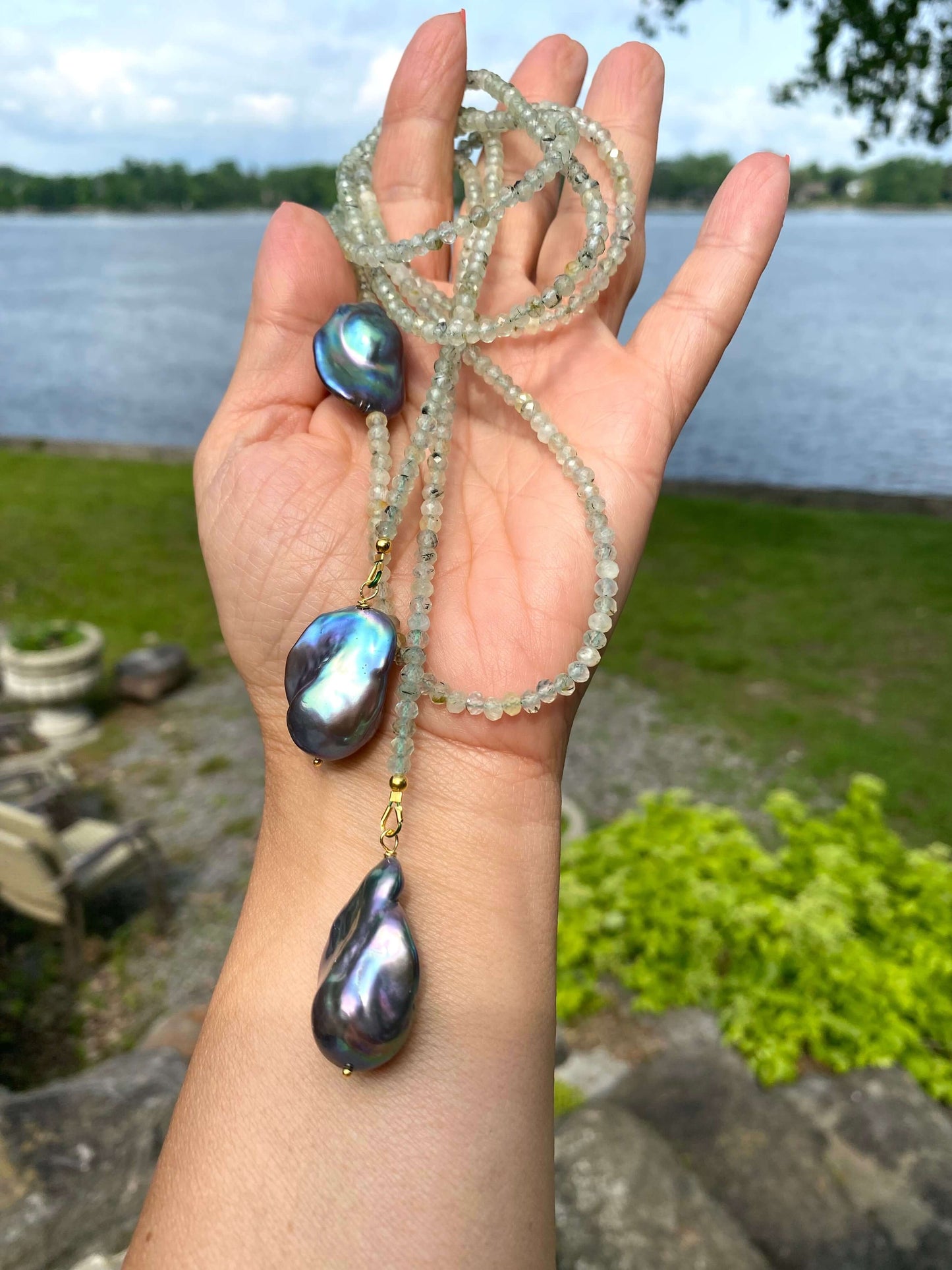 Green Prehnite and Black Baroque Pearls Lariat Necklace held outdoors by a hand, showcasing its elegance and craftsmanship.