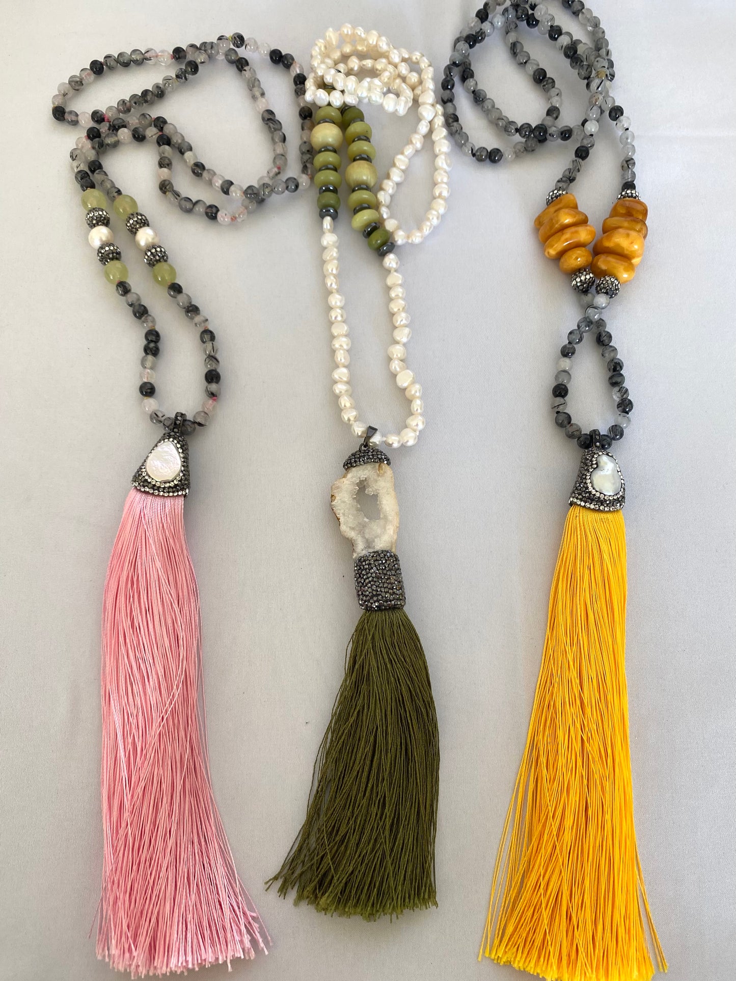 Rutilated quartz necklaces with yellow, pink, and green tassels displayed on white table.