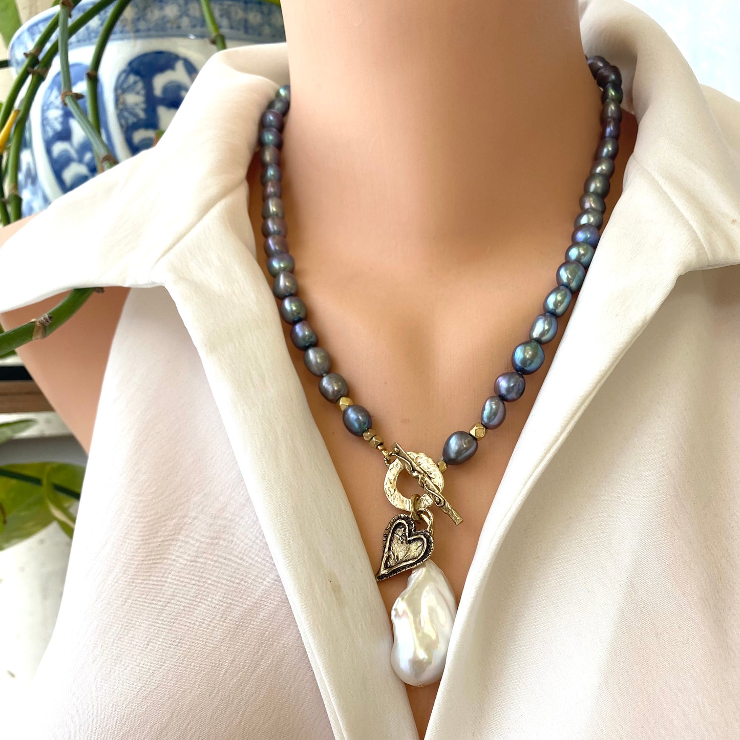Black pearl baroque pearl necklace worn at the neckline with white baroque pearl pendant and gold bronze toggle clasp
