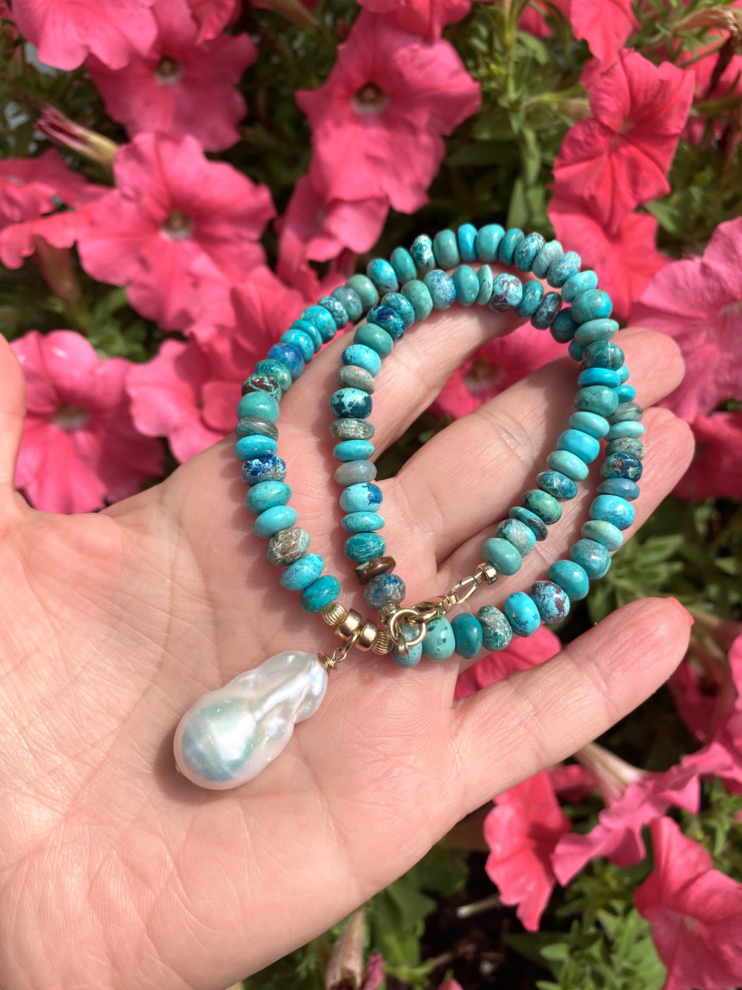 Handcrafted turquoise pearl necklace featuring Arizona turquoise and baroque pearl, set against vibrant pink flowers.