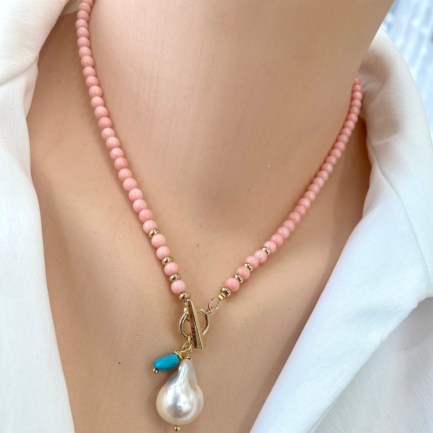 Pink coral toggle necklace with baroque pearl and turquoise charm worn on a mannequin neck.