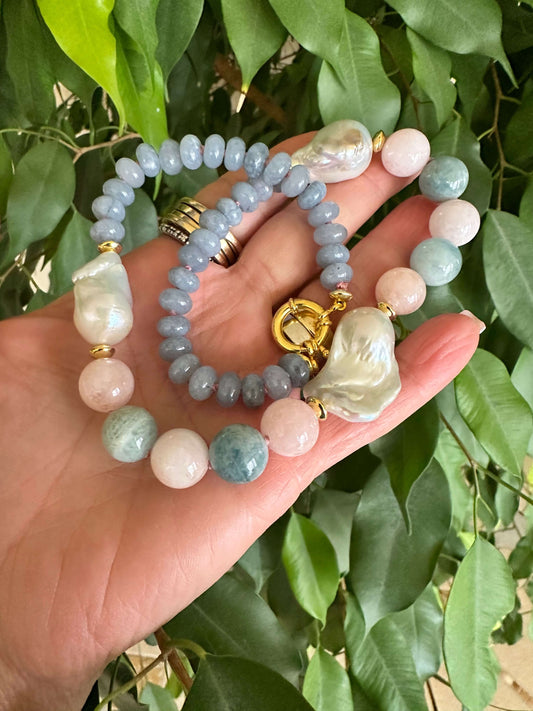 Blue jade morganite aquamarine pearl necklace showcasing baroque gem design, held in hand among lush foliage.