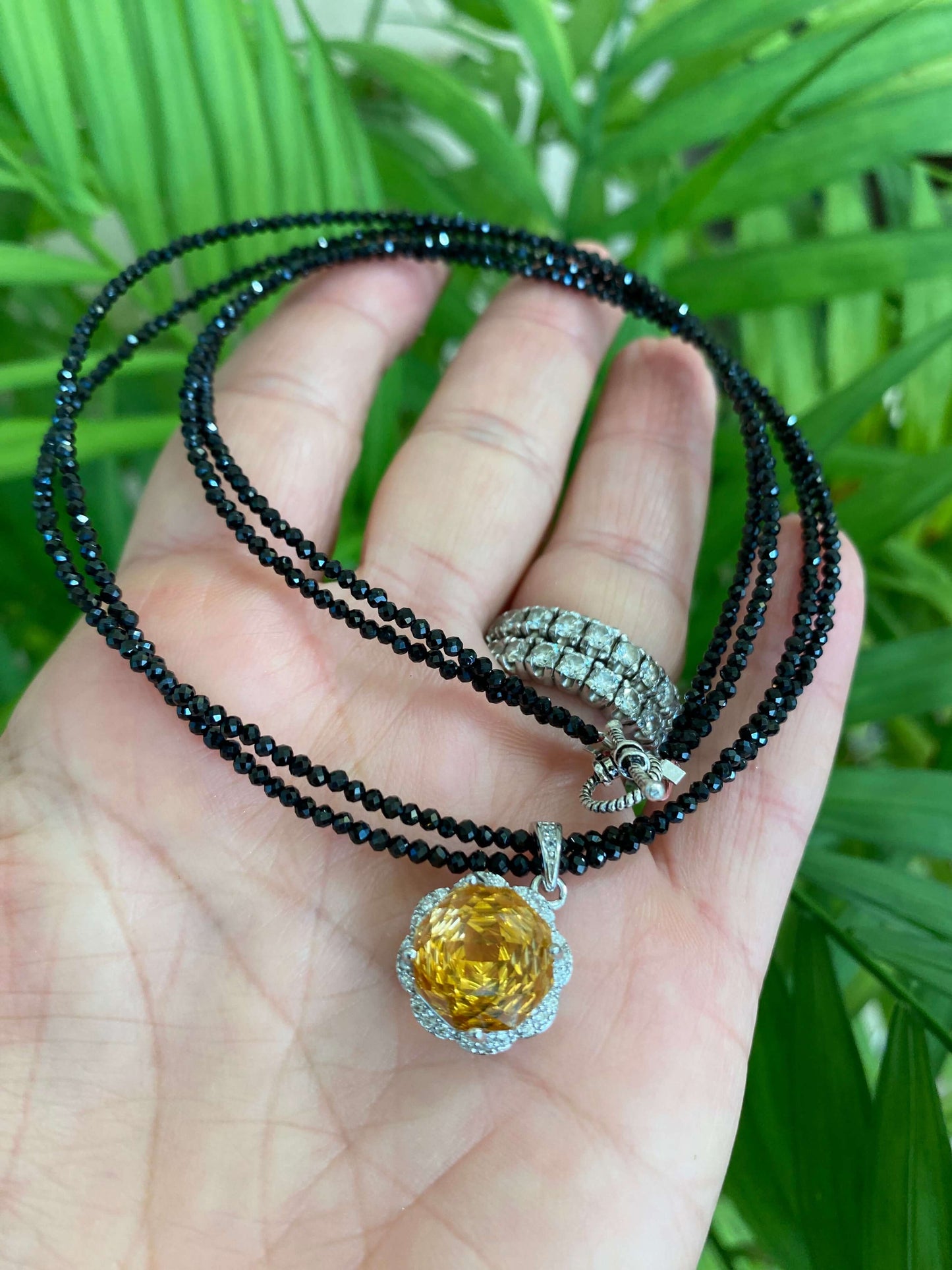 Hand holding black spinel and citrine pendant necklace near green leaf background