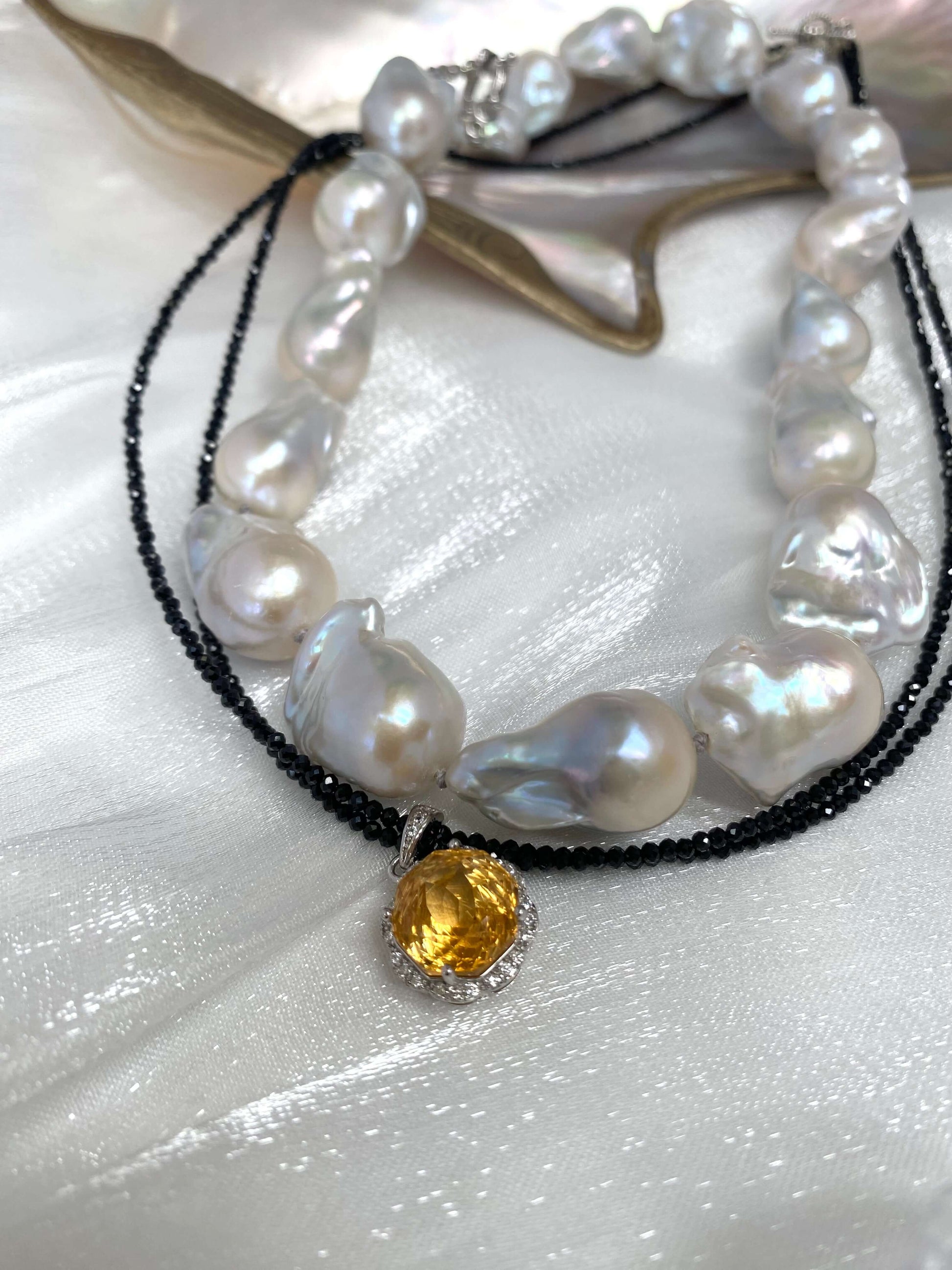Black spinel and citrine pendant necklace displayed beside baroque pearl necklace