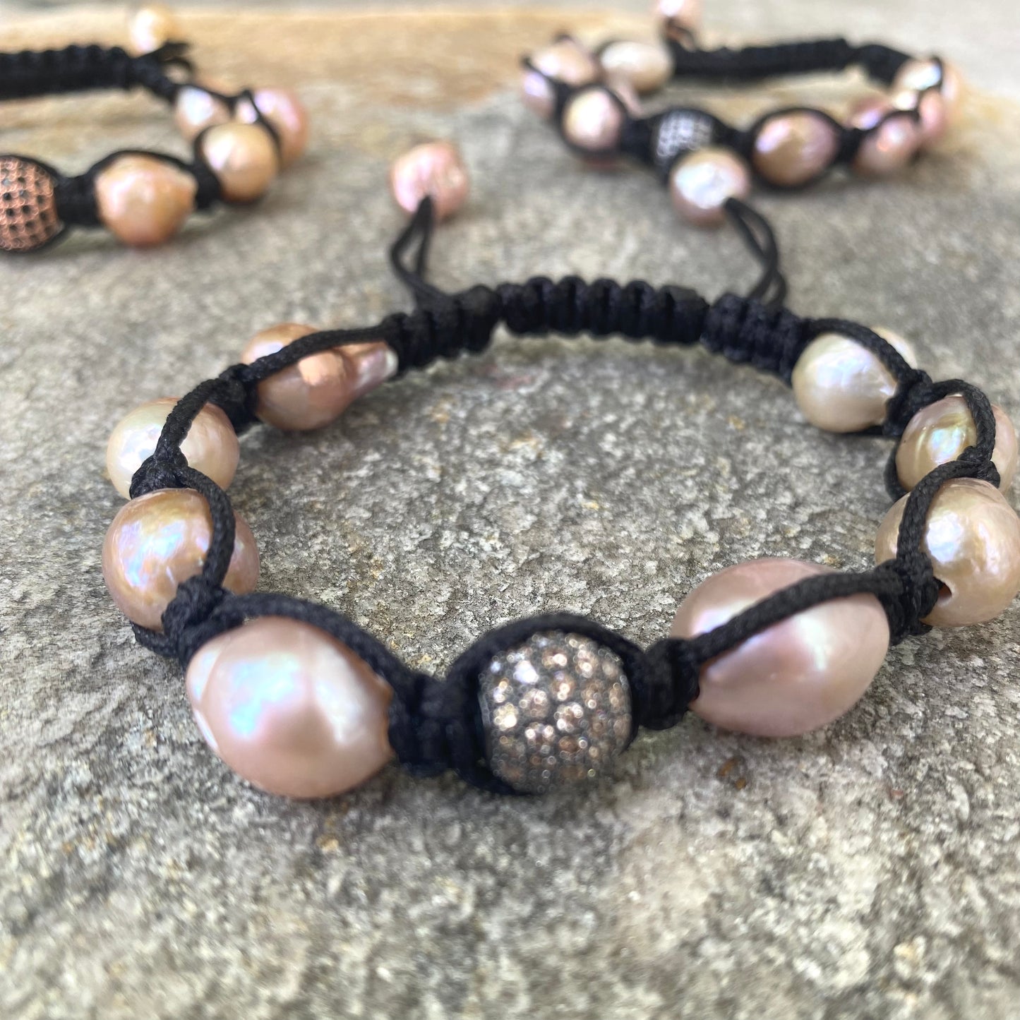 Baroque pearl bracelet featuring pastel pearls and black thread on textured background.