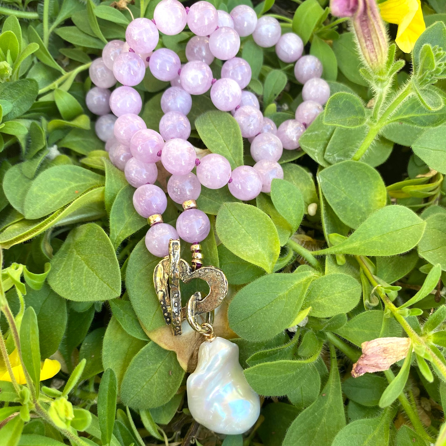 Kunzite toggle necklace with baroque pearl pendant displayed among vibrant green foliage.