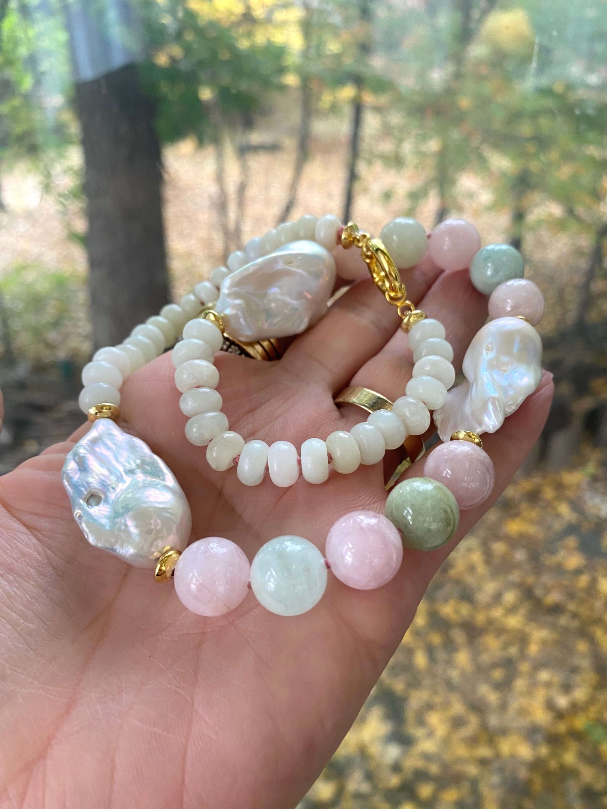 Detailed view of handmade morganite and jade necklace with baroque pearls held outdoors, highlighting pastel gemstone tones.